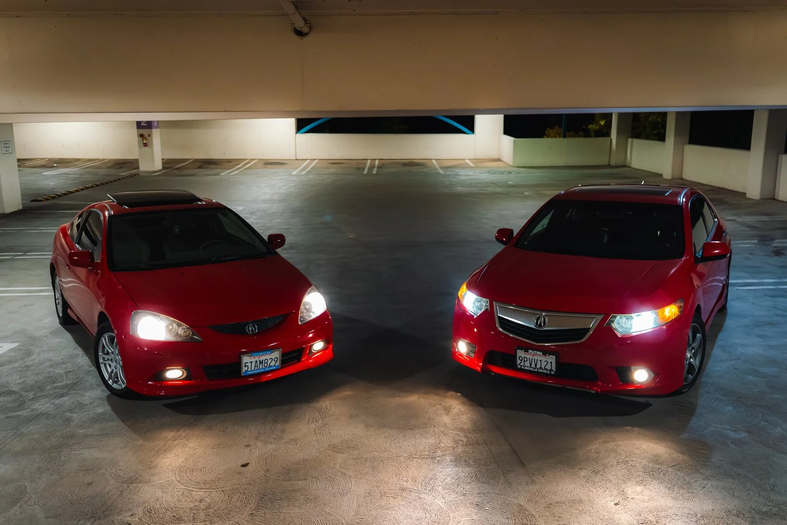 Two red cars parked side by side in an indoor parking garage at night.