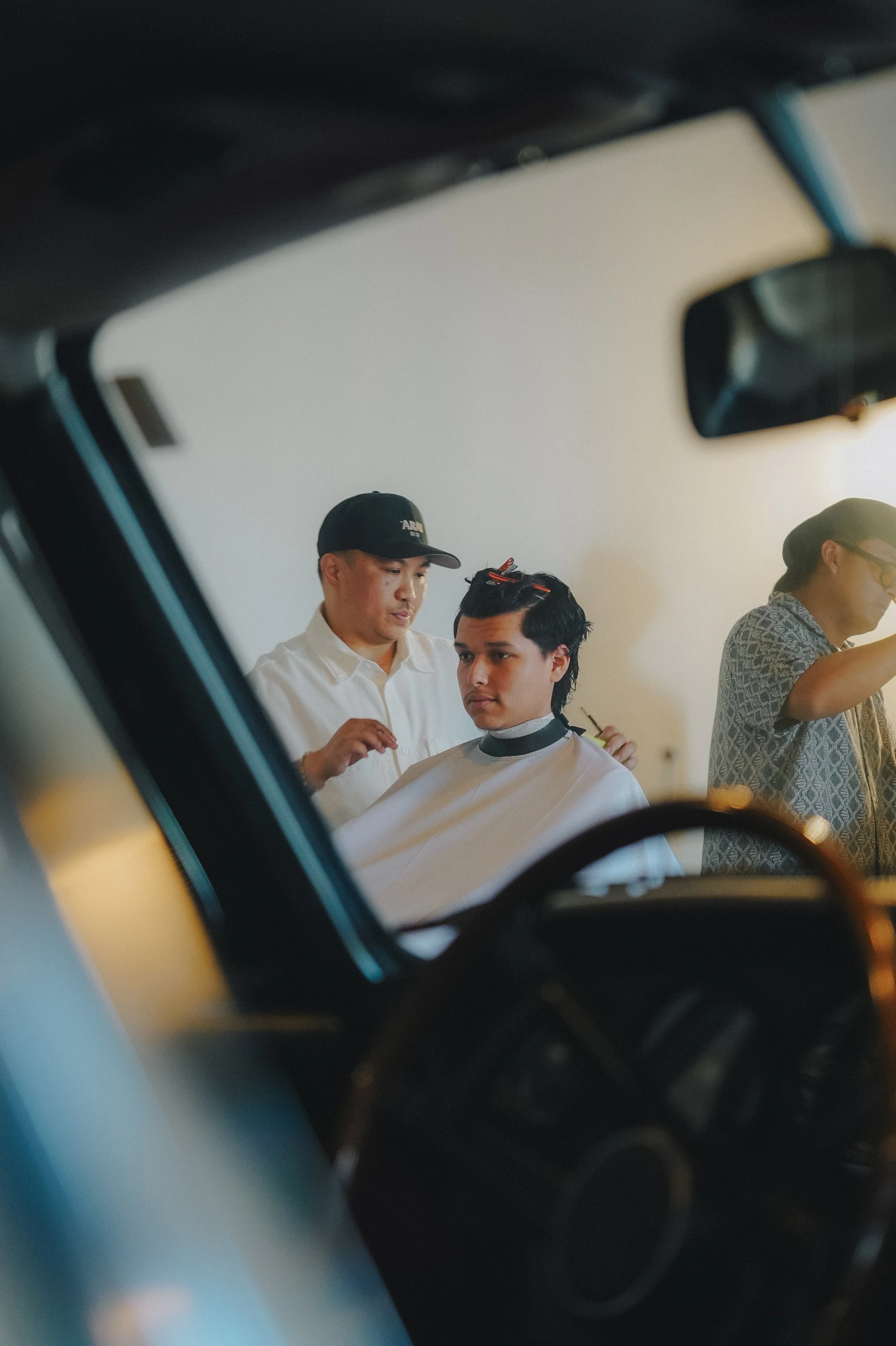 A person getting a haircut at a salon with a stylist working on his hair. The image is viewed from inside a car, through the window.