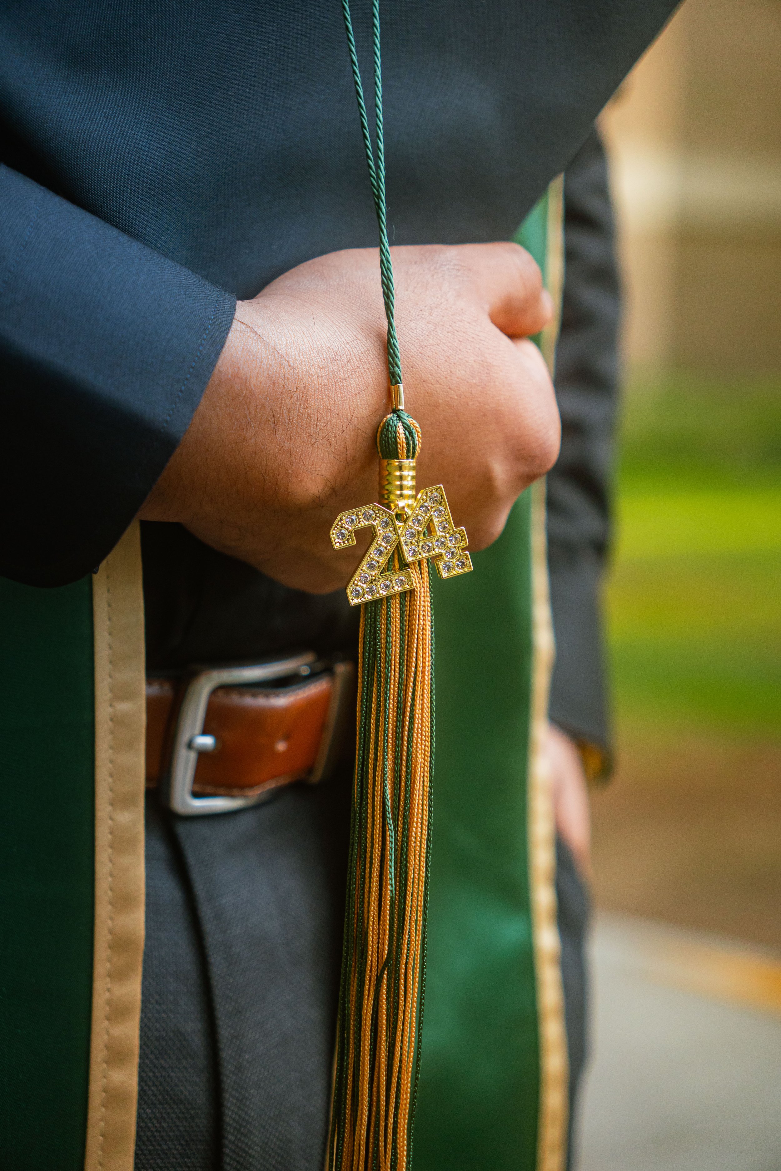 A graduate wearing a black cap and gown with a green and gold tassel also featuring a gold '24' pendant.