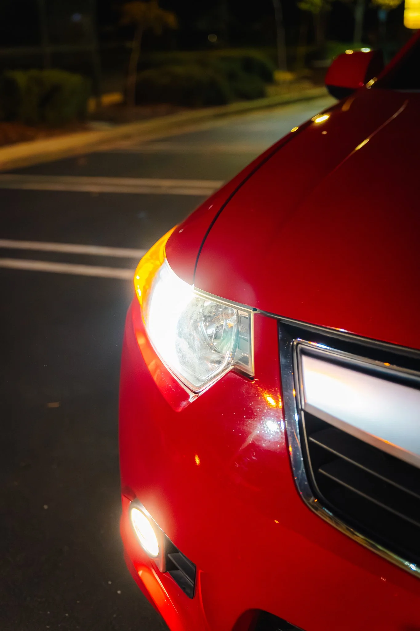 Close-up of a red car with illuminated headlights and part of its front grille, taken at night.