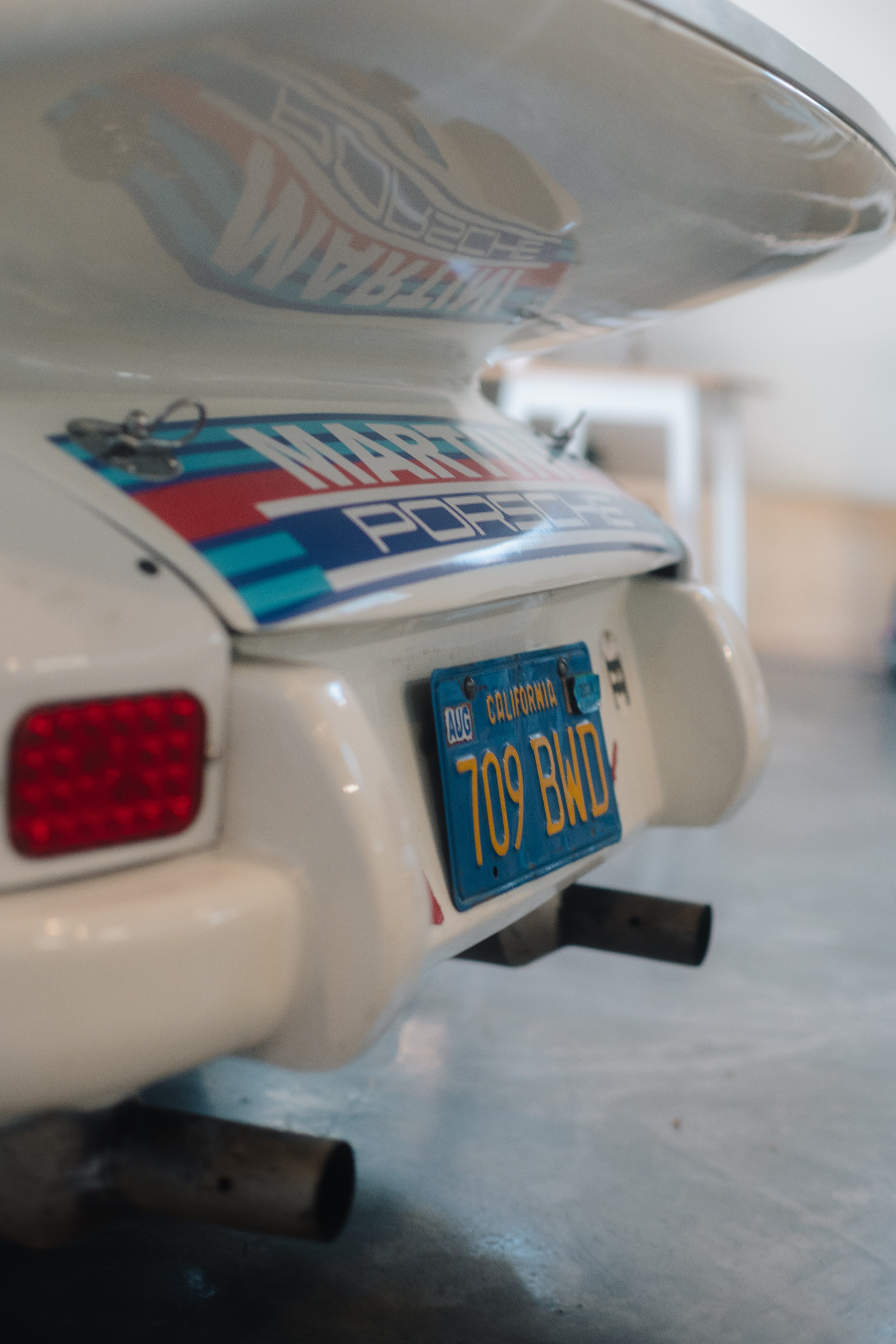 Rear view of a white miniature car with a California license plate reading '709 BND' and a Harley-Davidson sticker on the trunk, parked indoors.