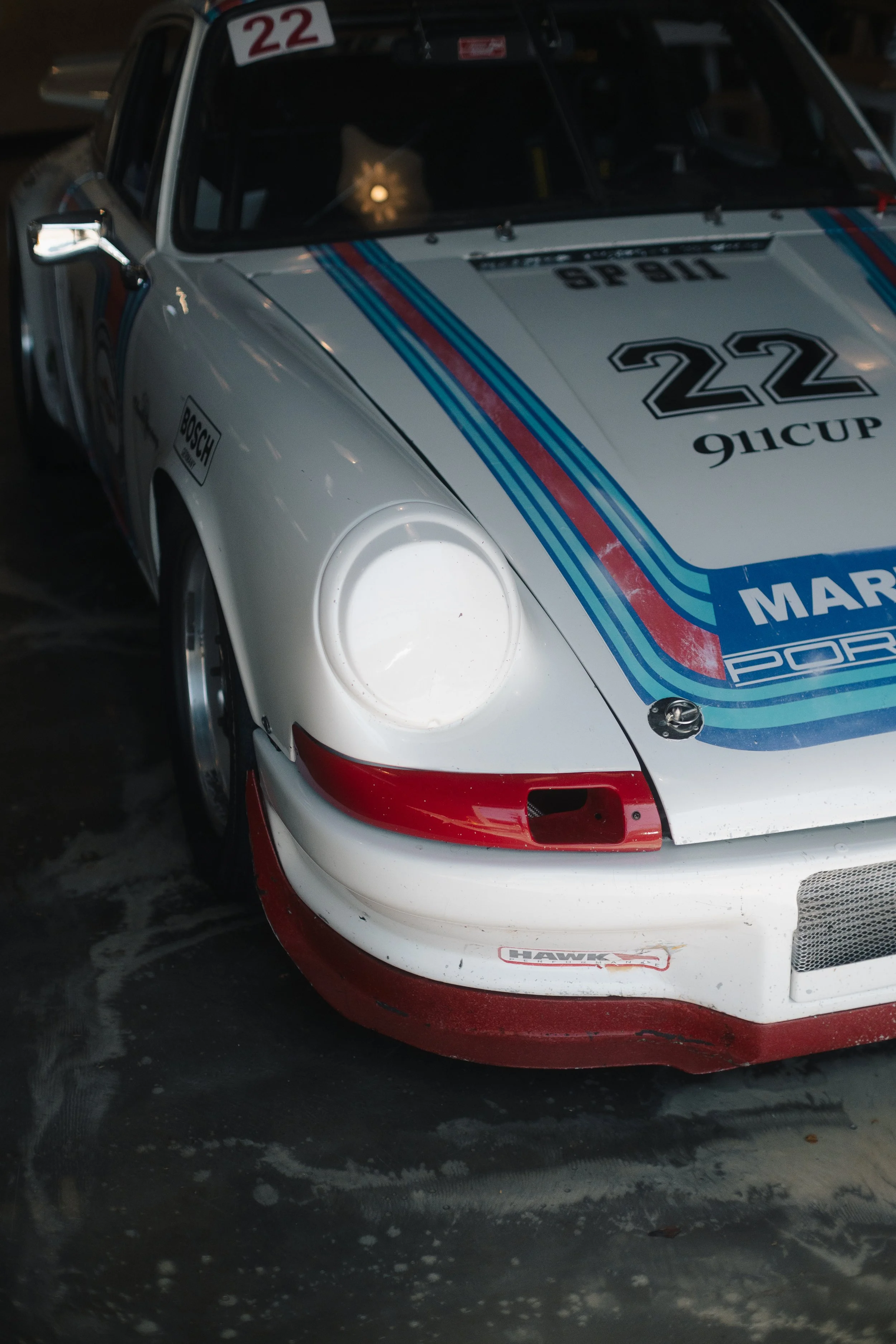 Close-up of a white race car with racing stripes and number 22, parked on a wet surface.