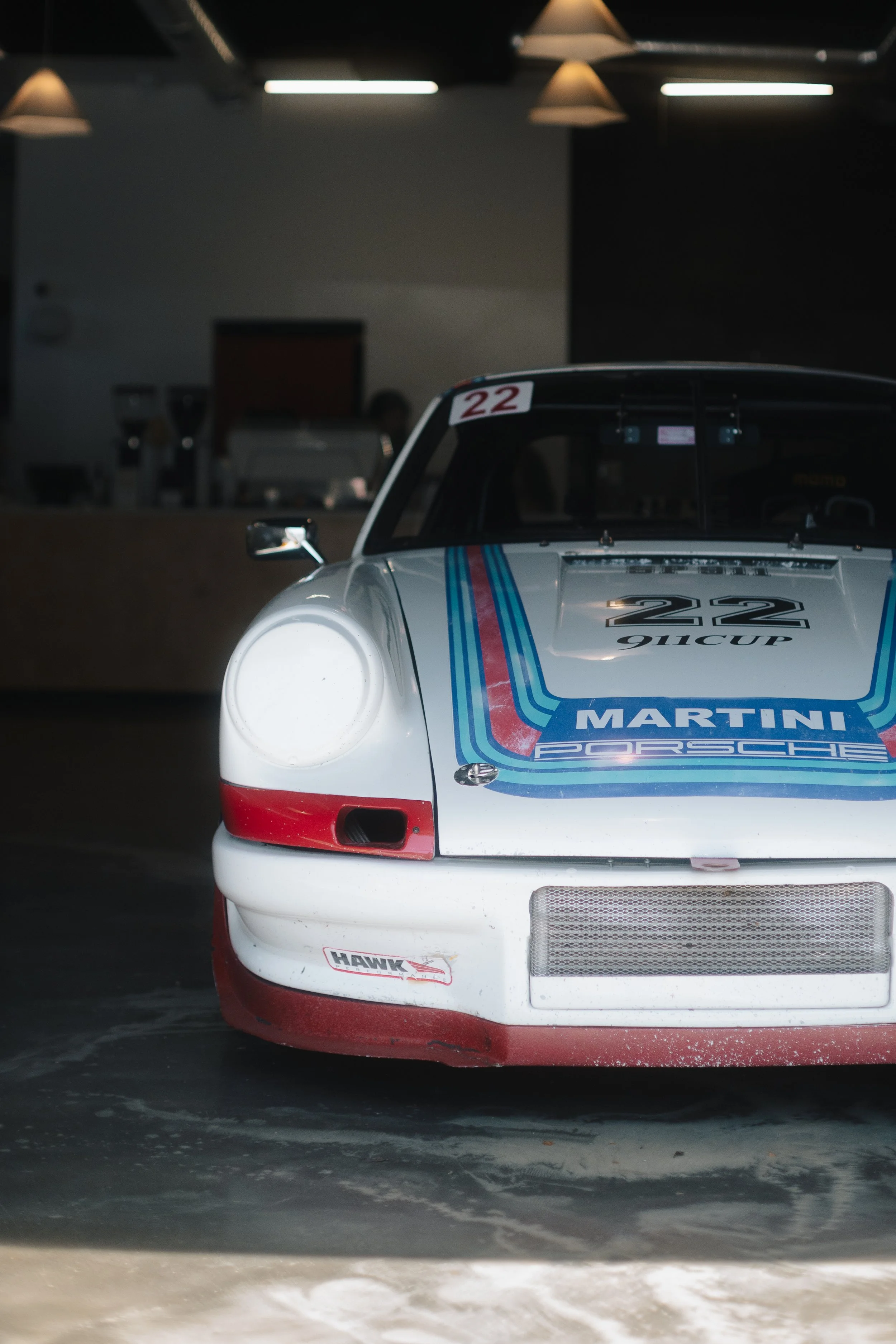 The front of a classic Porsche racing car with a white body, racing stripes, and the number 22, parked indoors.