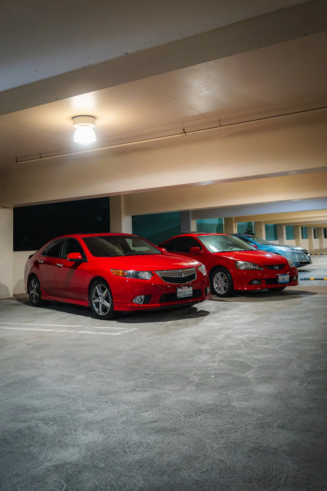 Underground parking garage illuminated by ceiling lights, with a red Honda Civic and other cars parked.