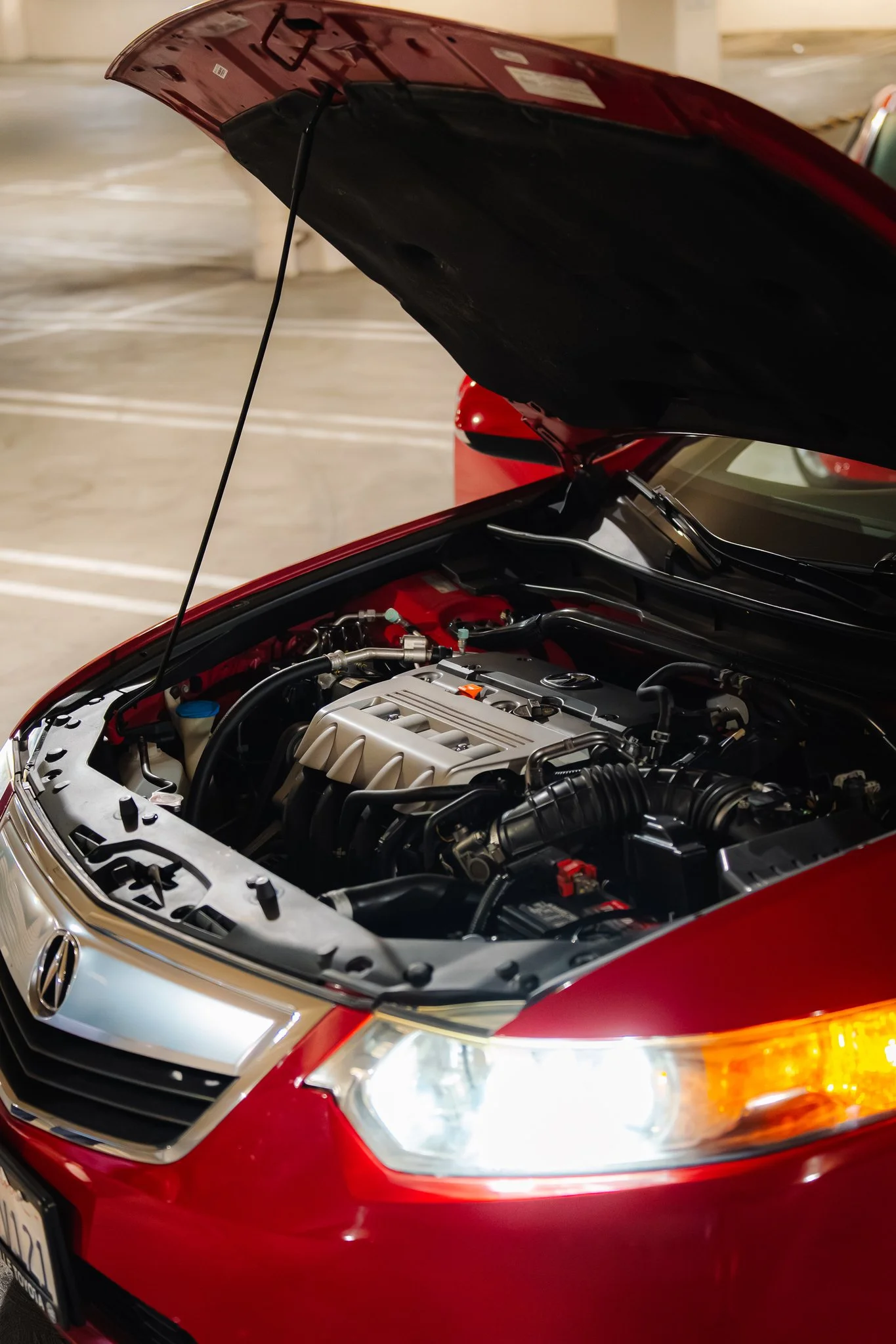 Close-up view of a red car with its hood open, exposing the engine and various components inside the engine bay.