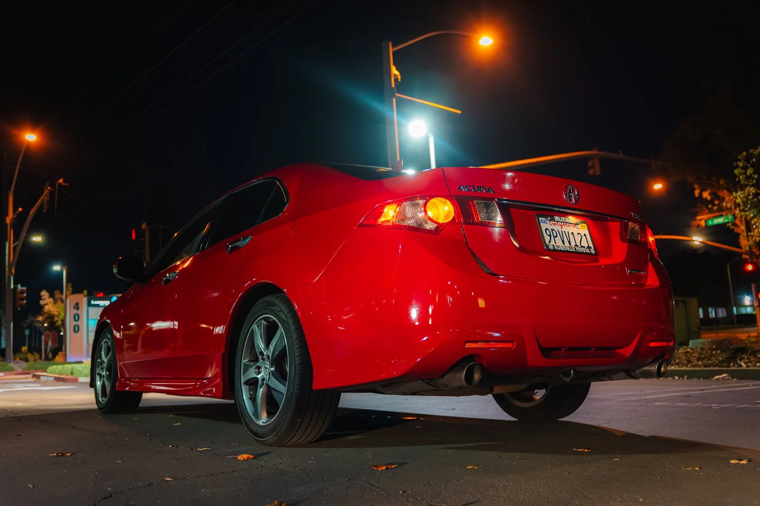 A red Acura sedan parked at night under streetlights with visible license plates.