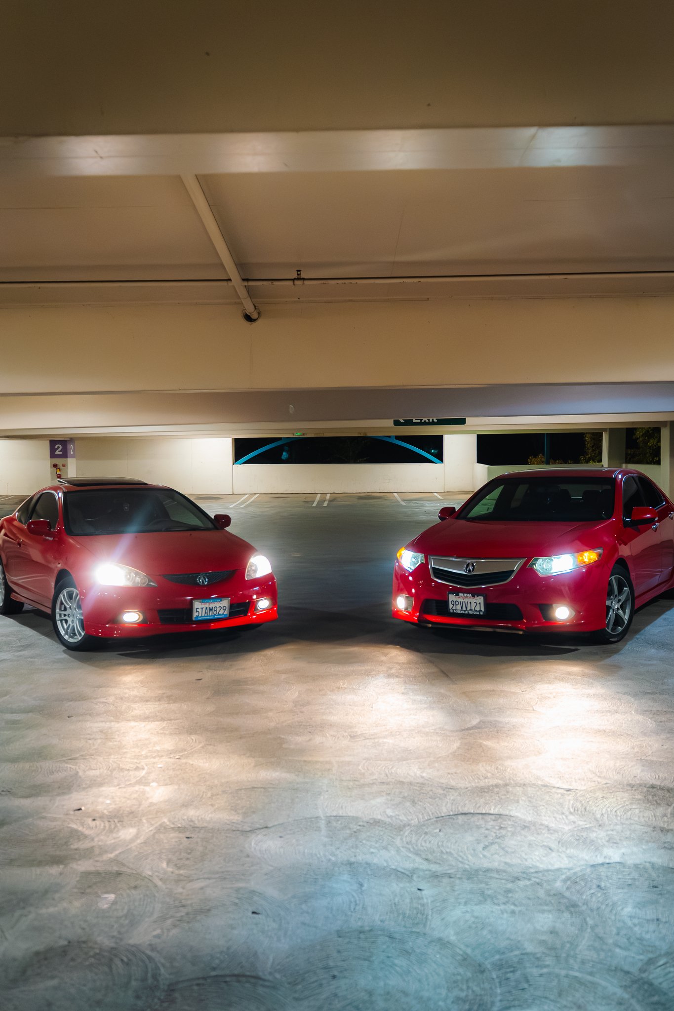 Photo of two red cars parked in an indoor parking garage with a concrete floor and ceiling.
