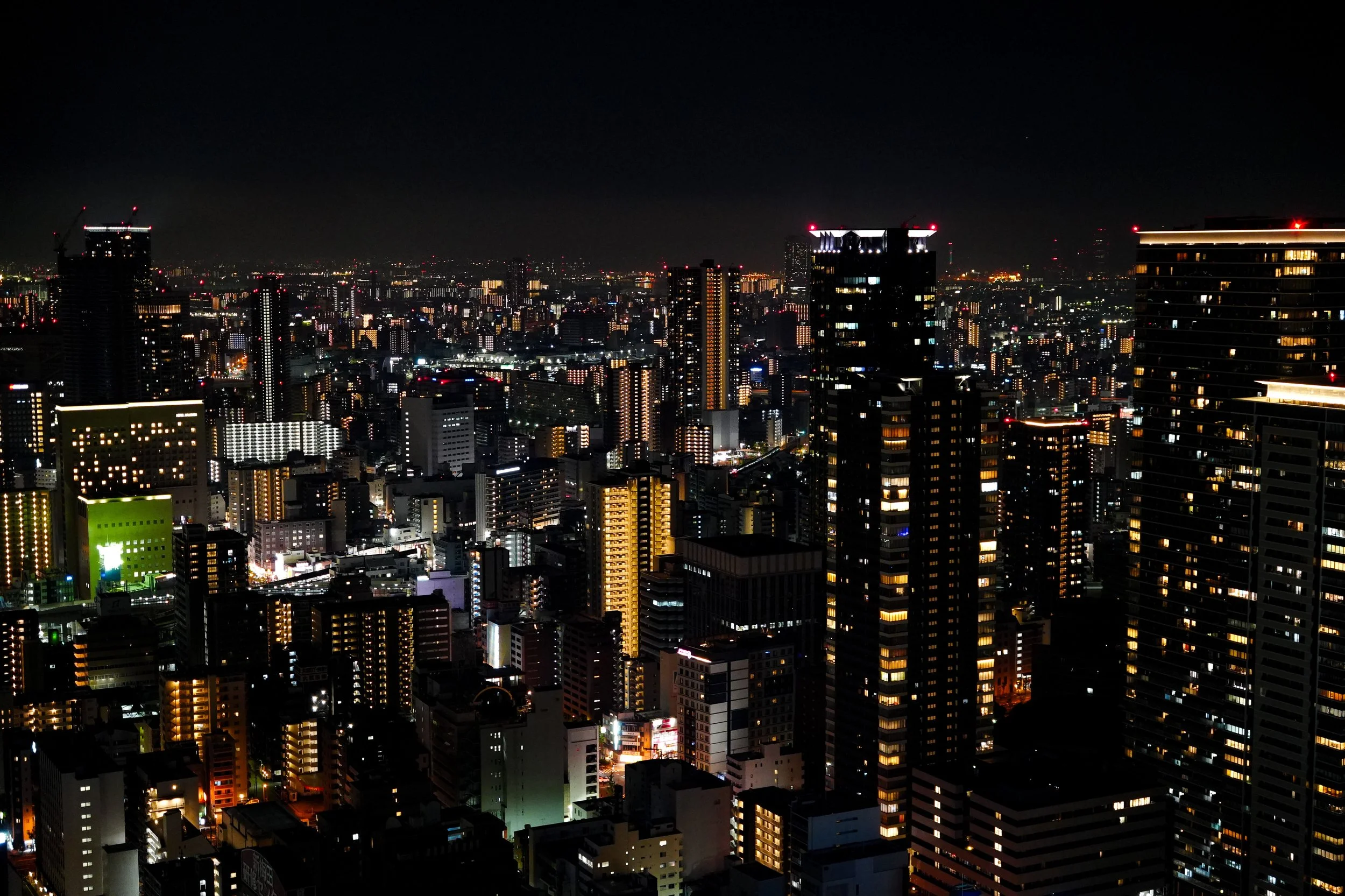 Nighttime cityscape with numerous illuminated high-rise buildings and skyscrapers in a modern urban area.