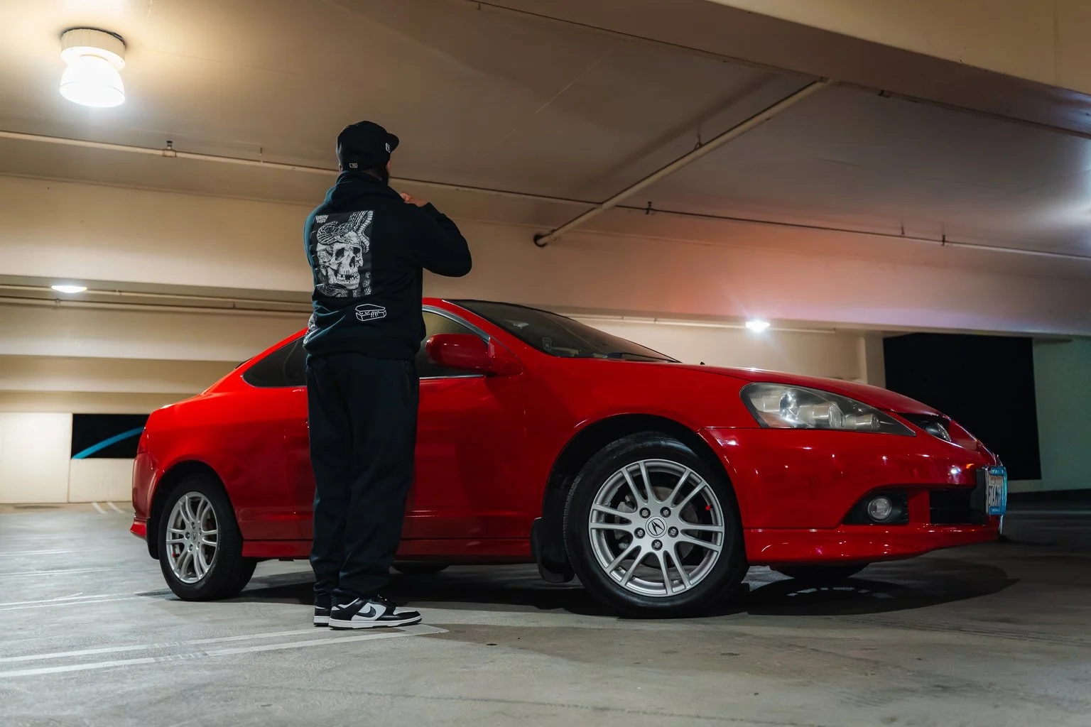 A person standing in a parking garage beside a red sports car.