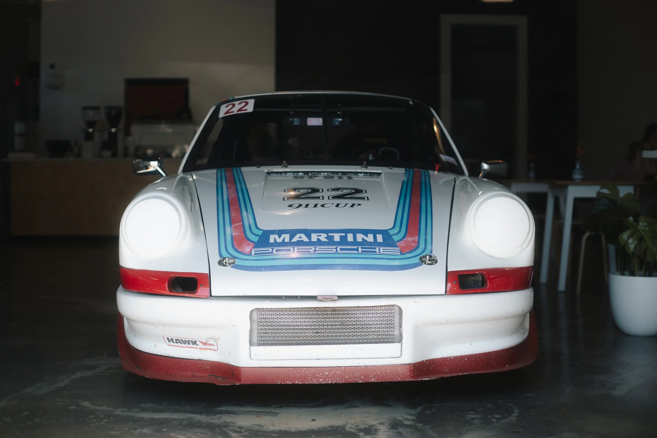 A white Porsche race car with Martini Racing livery and the number 22, displayed indoors in a dimly lit setting.