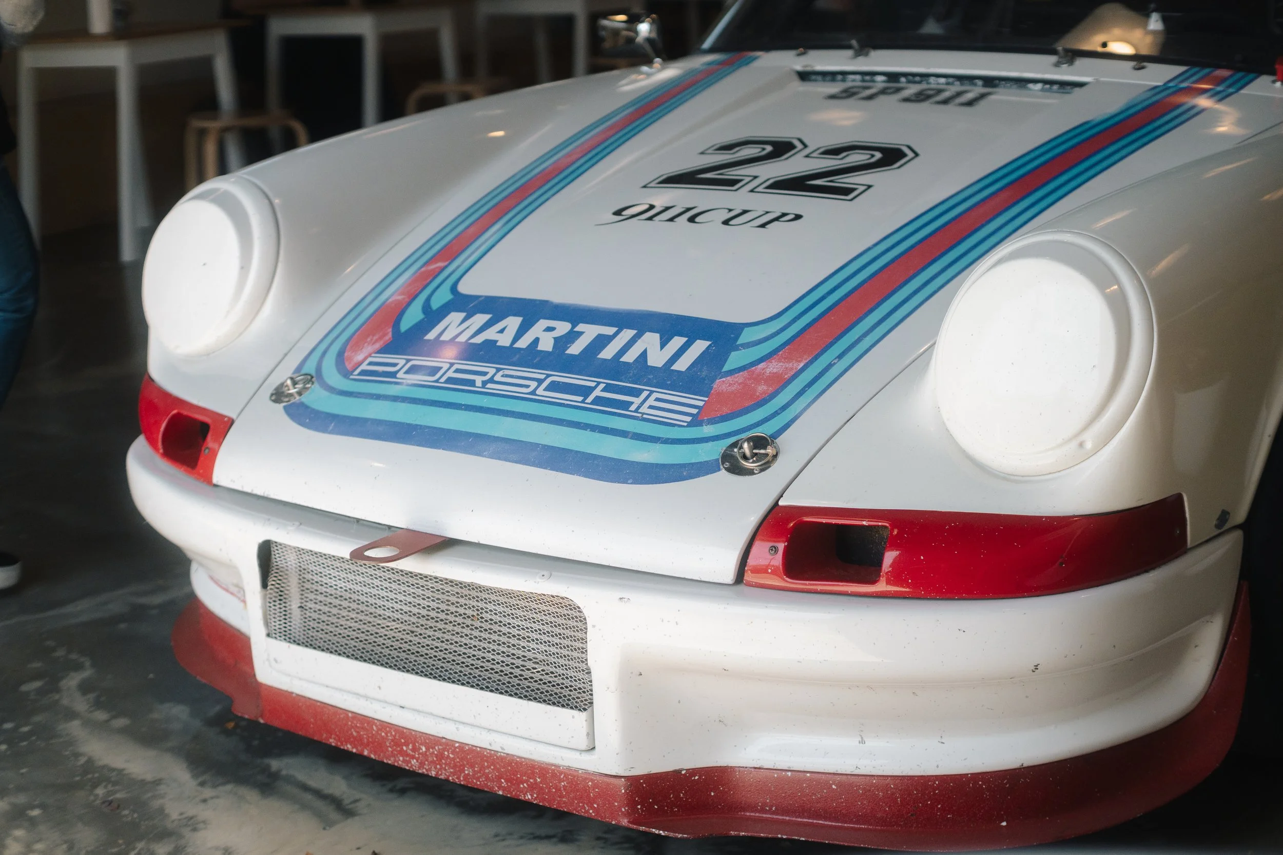 Close-up of a white race car with Martini and Porsche branding, number 22, with red and blue racing stripes.