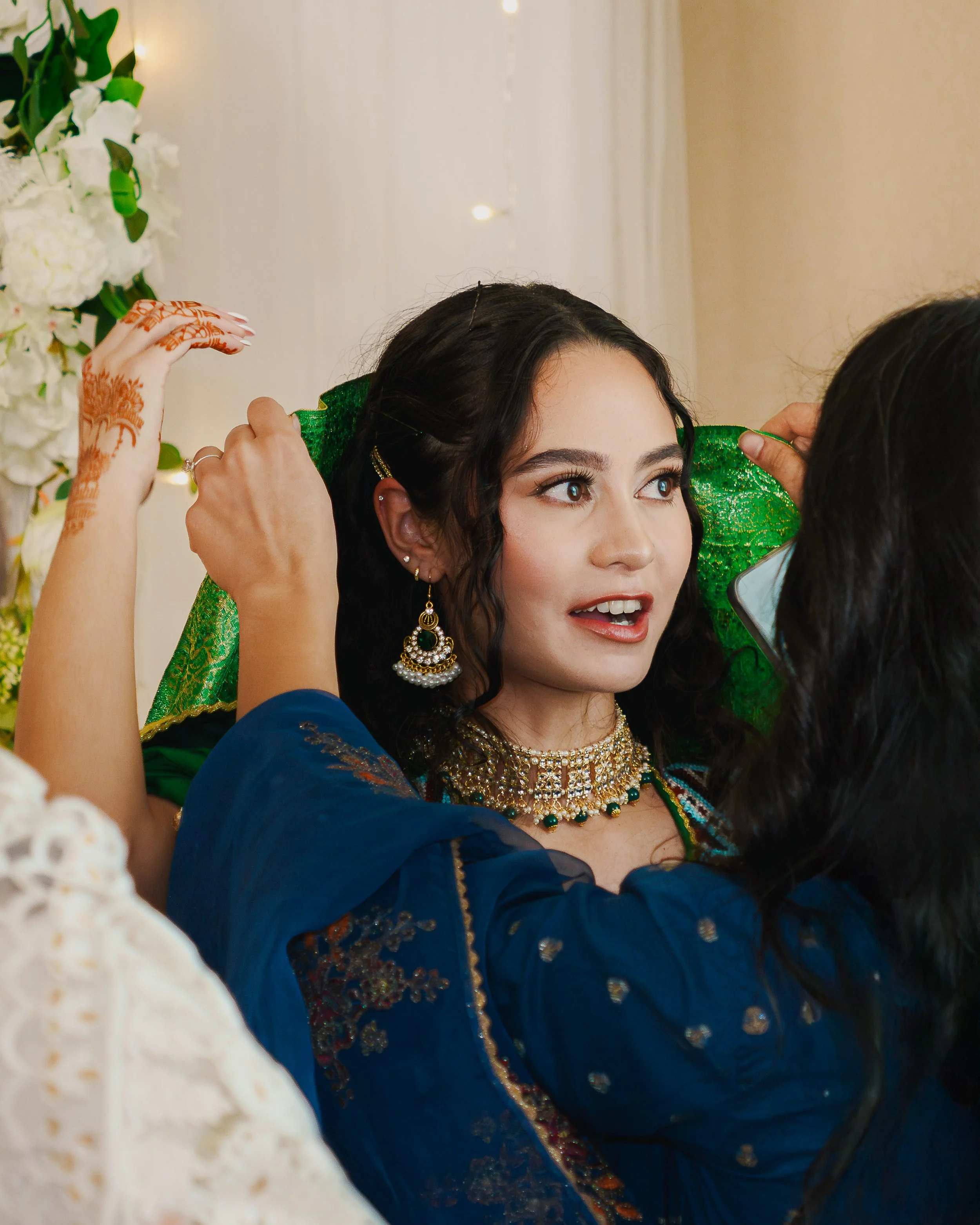 A young woman dressed in traditional Indian attire, with intricate jewelry, celebrating a special occasion as she adjusts her outfit.