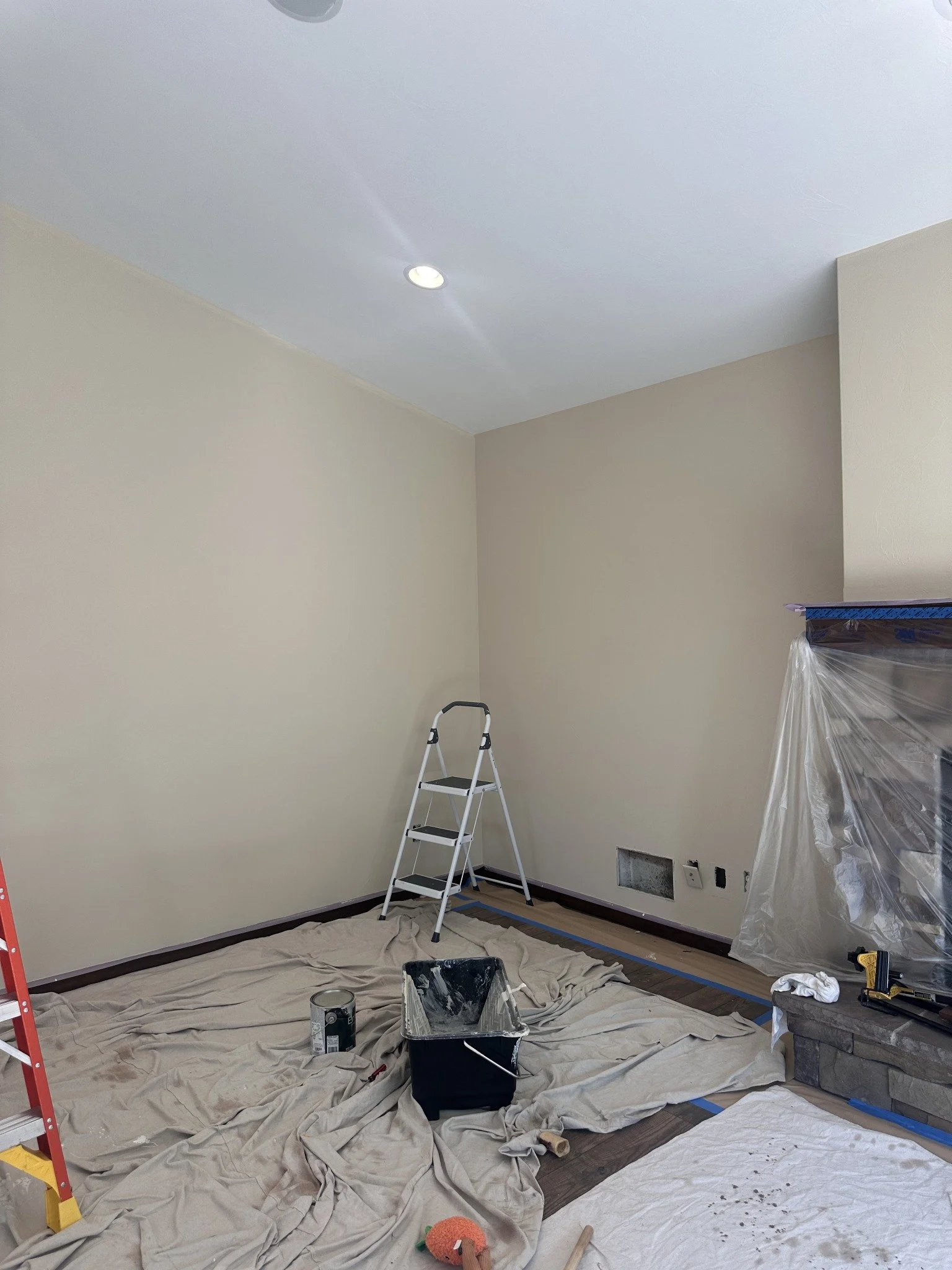 Interior painting project showing light walls, recessed ceiling lights, and protected flooring.