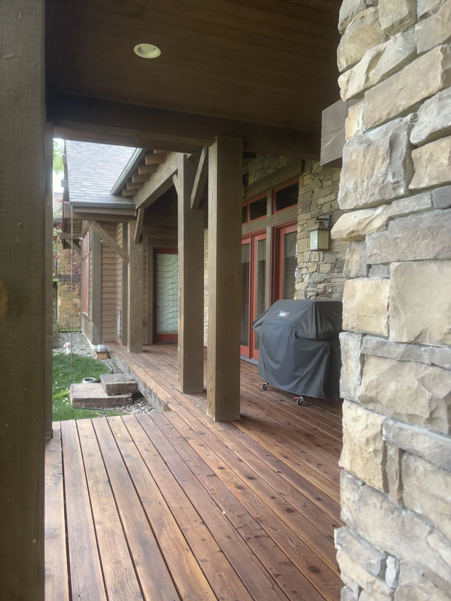 Deck restoration project showing wood grain on a covered porch beside stone columns.
