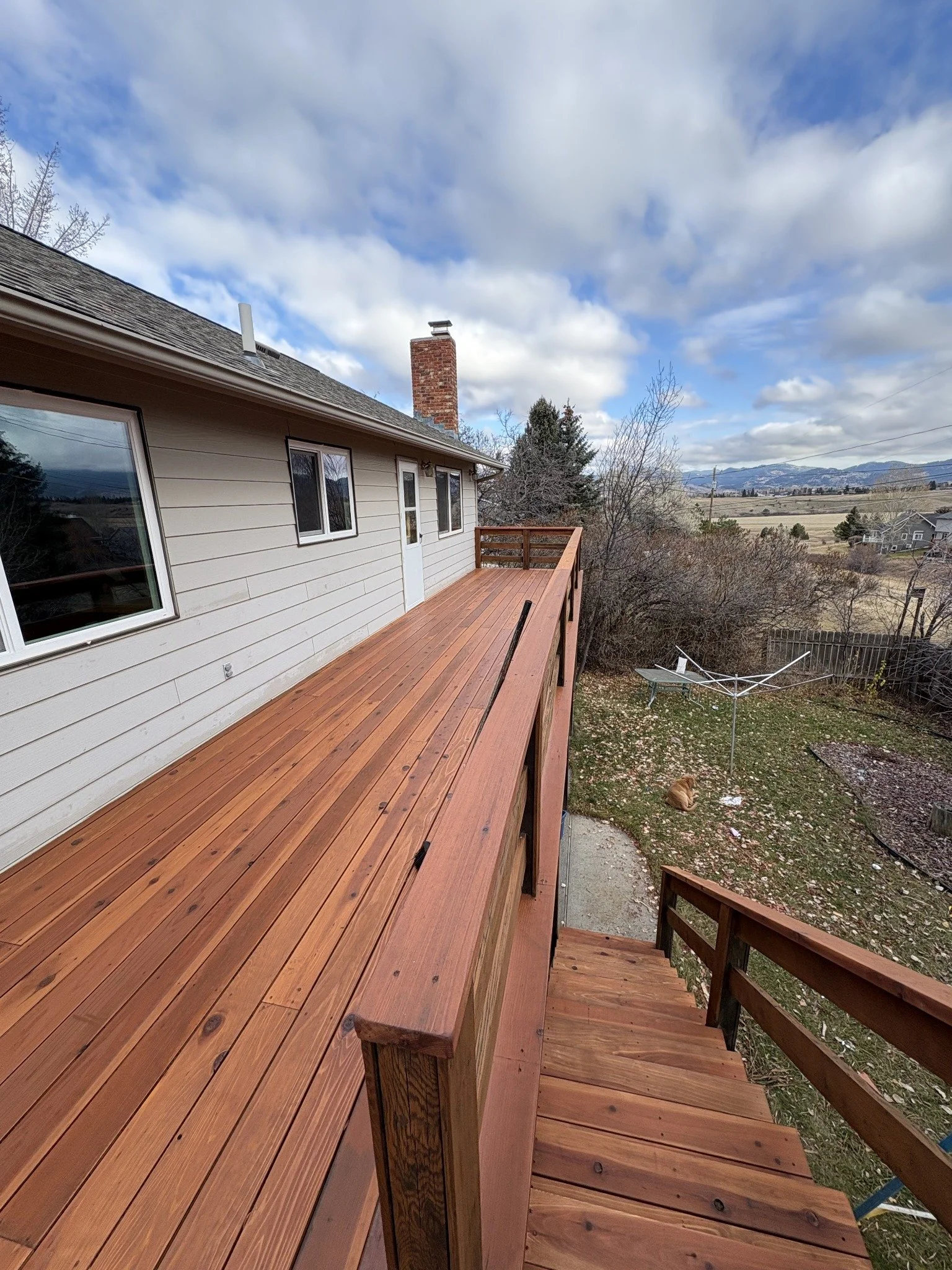 Deck restoration project showing a long wood deck with matching railings beside white siding.