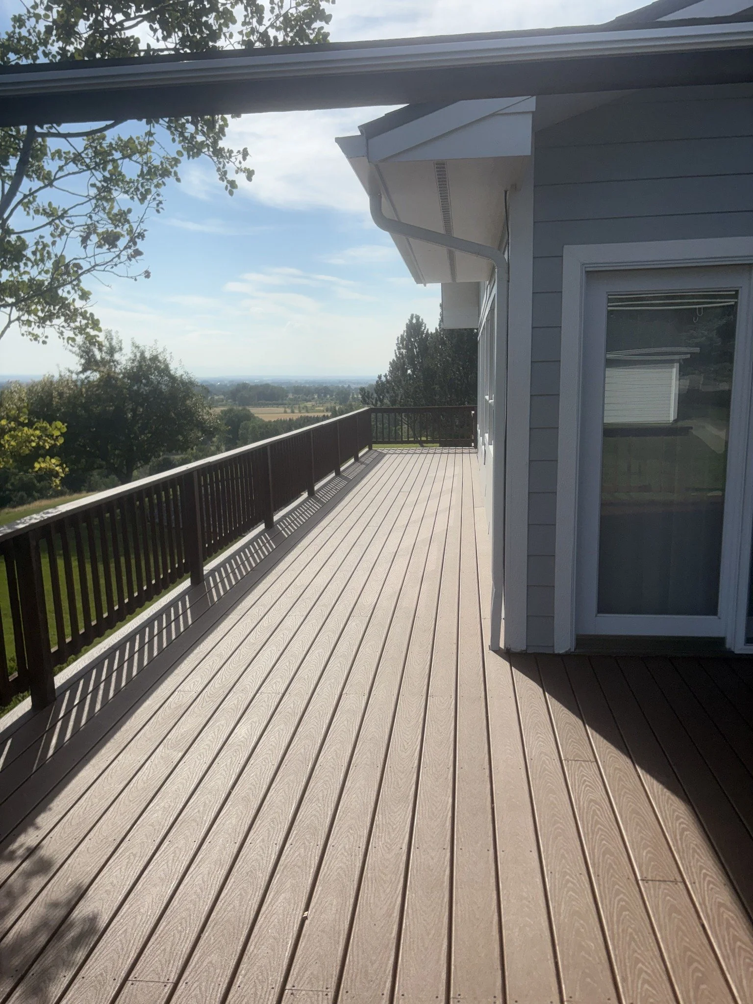 Deck building and repairs project showing long gray deck boards beside a house and dark railing.