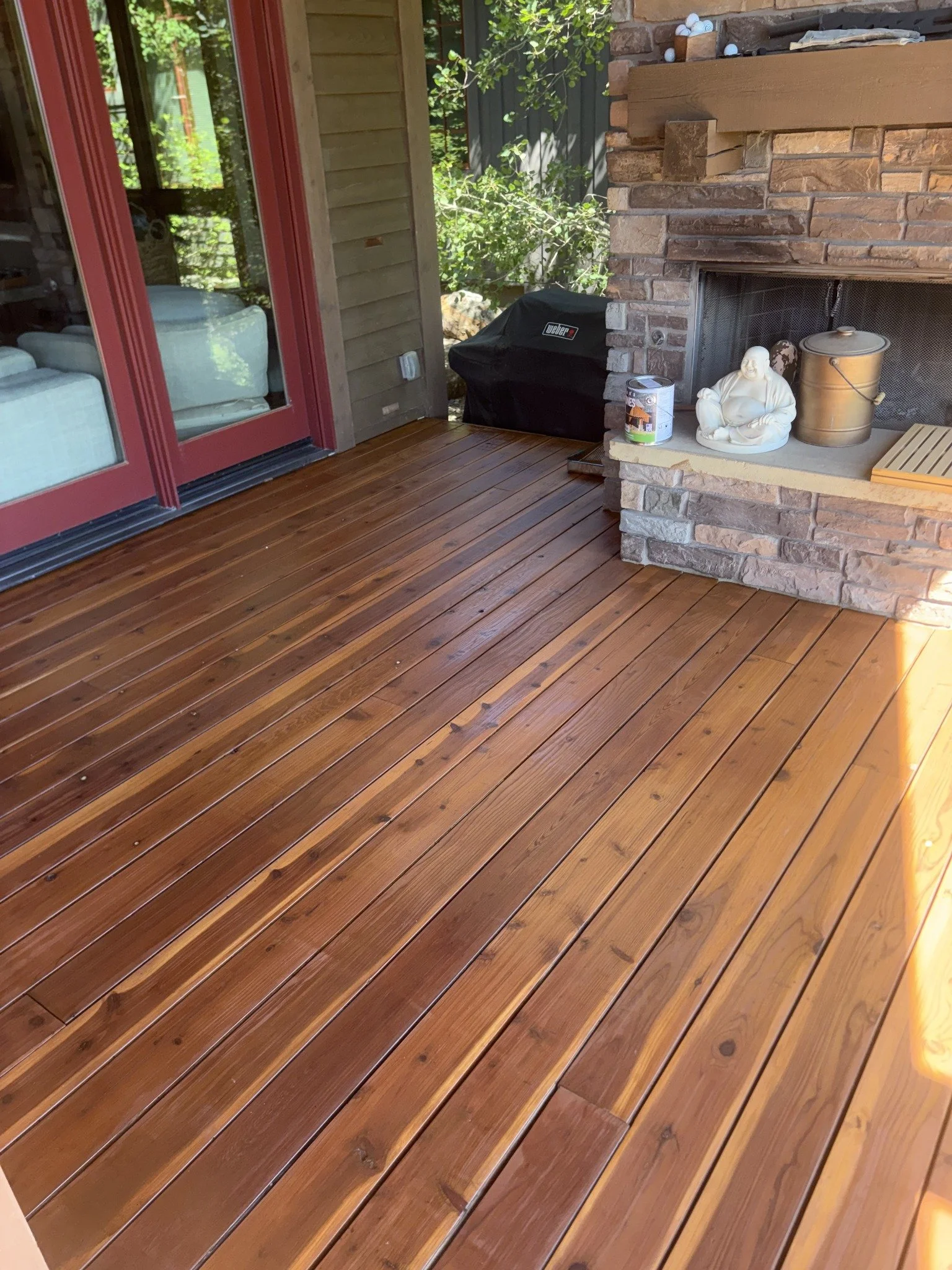 Deck restoration project showing stained wood boards beside a stone fireplace and red door.