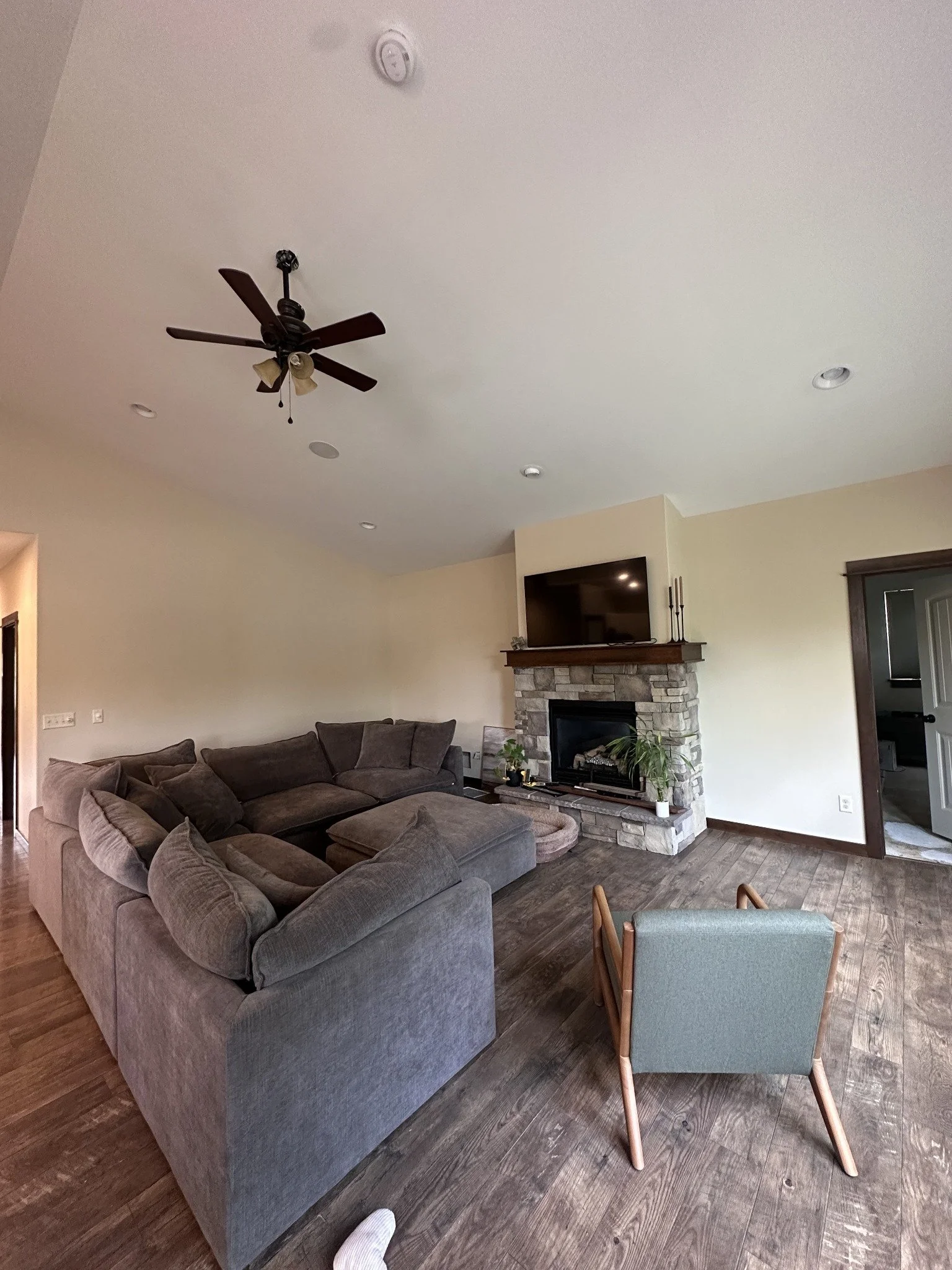 Interior painting project with light walls, a white ceiling, ceiling fan, and stone fireplace.