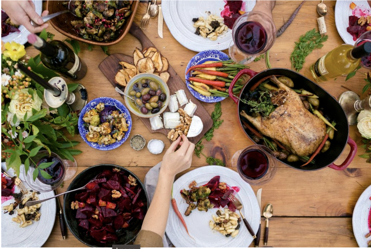 wooden table covered with abundant of foods including beets, carrots, caulifower, olives, cheese and more
