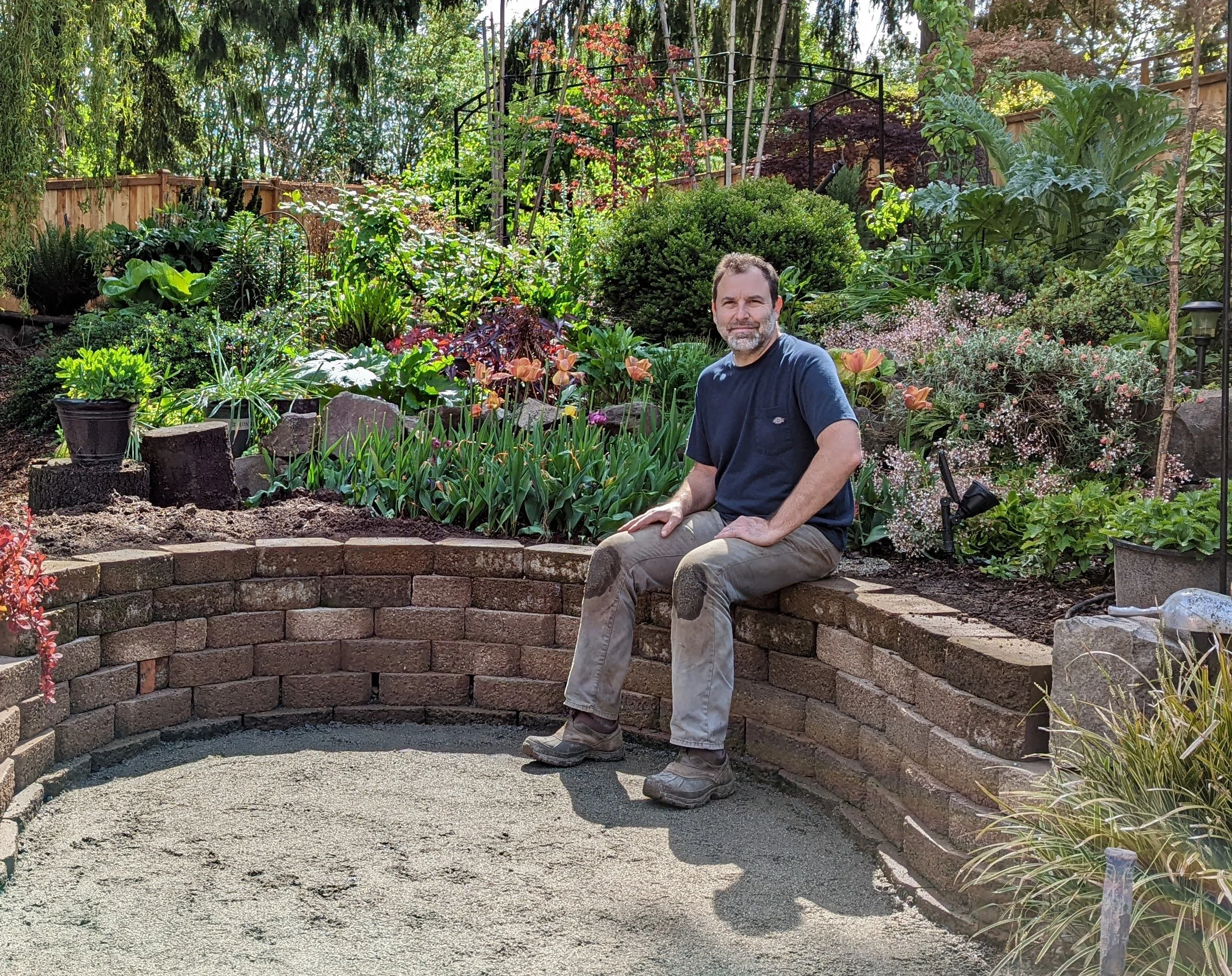 Christopher seated on a garden wall with a lovely garden backdrop