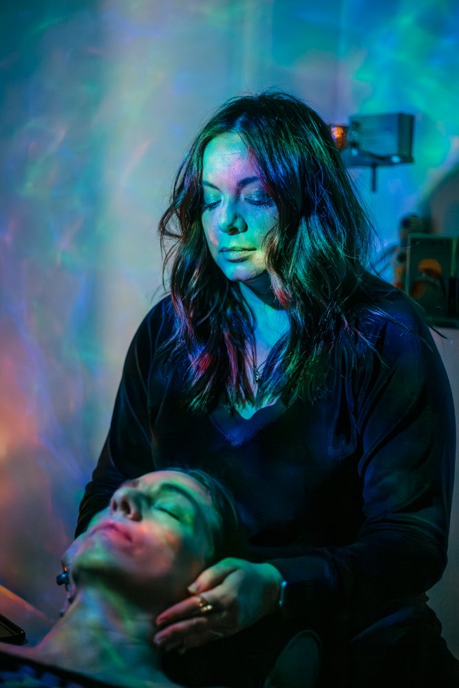 Woman performing a relaxing massage on another person, with colorful ambient lighting.