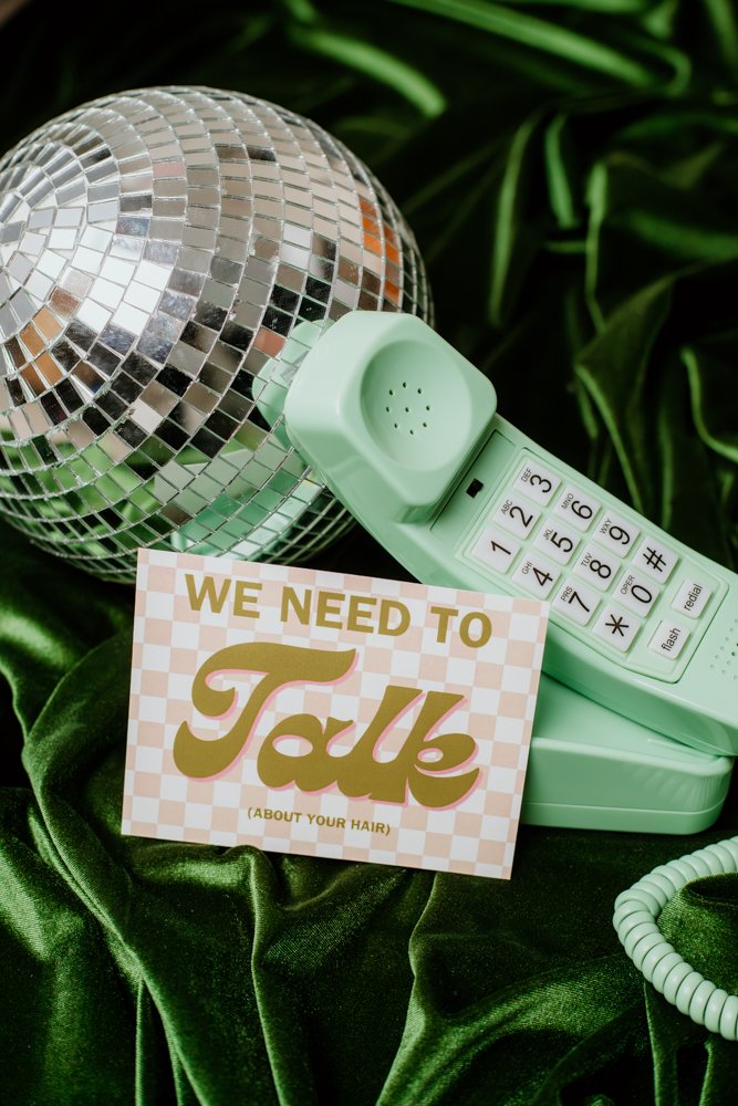 A retro green telephone and disco ball on green velvet with a card reading "We Need to Talk (About Your Hair)."