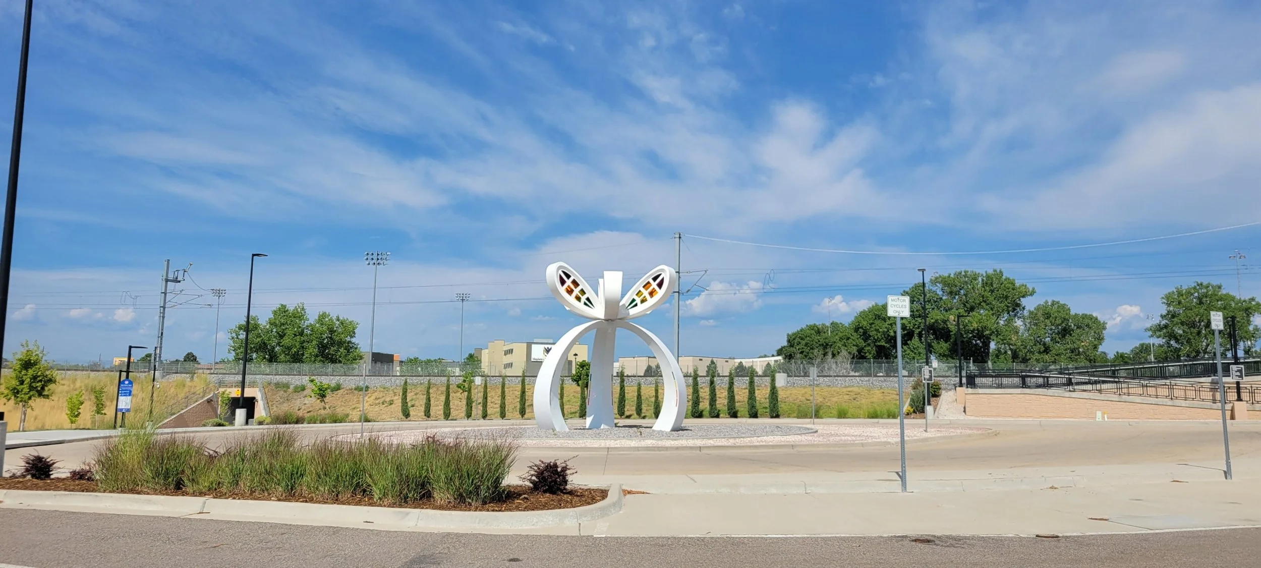 A decorative sculpture of a stylized butterfly or bow with colorful accents, situated in a roundabout with greenery and a clear blue sky in the background.