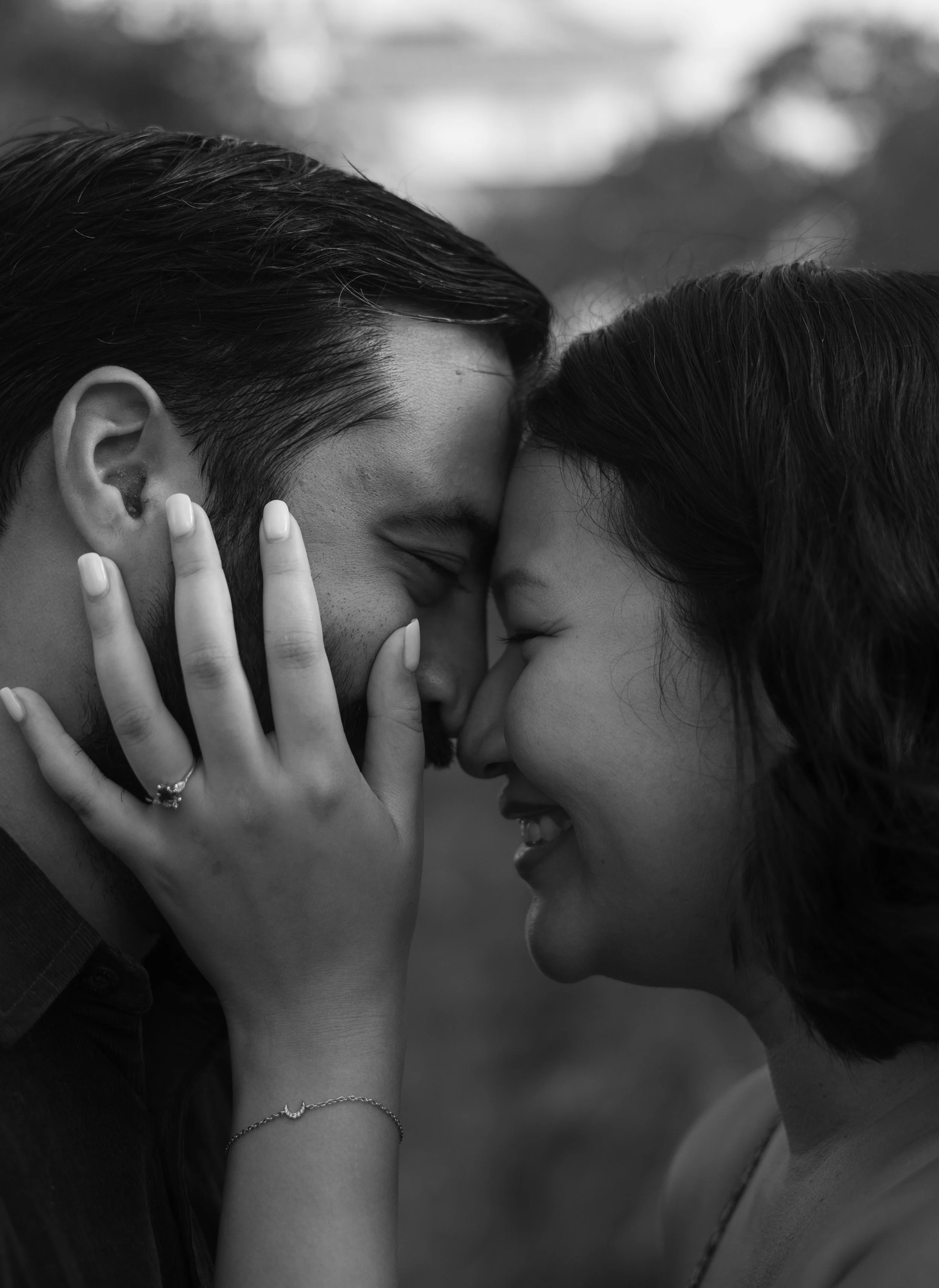 A black and white photograph of a young couple close together with foreheads touching and eyes closed, sharing an intimate moment.