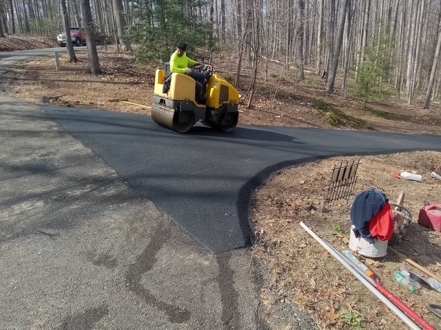 Worker operating a yellow road roller compacting fresh asphalt on a driveway