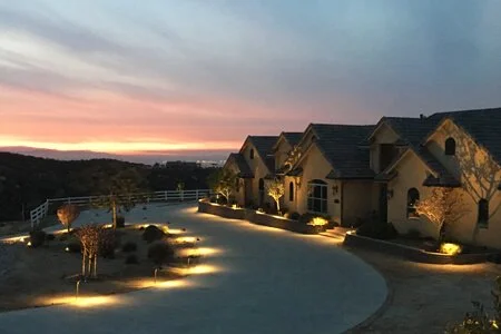 A suburban neighborhood at sunset with illuminated houses and landscaped yard.