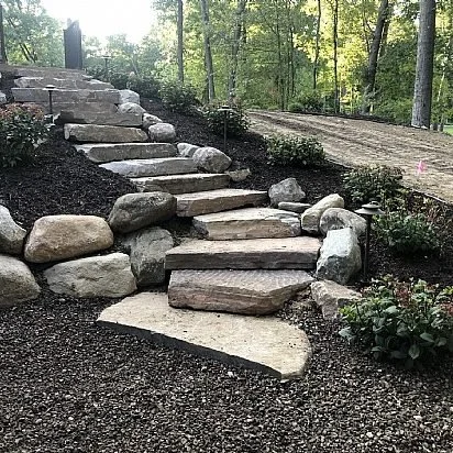 Stone steps leading up a landscaped backyard with plants and trees in the background.