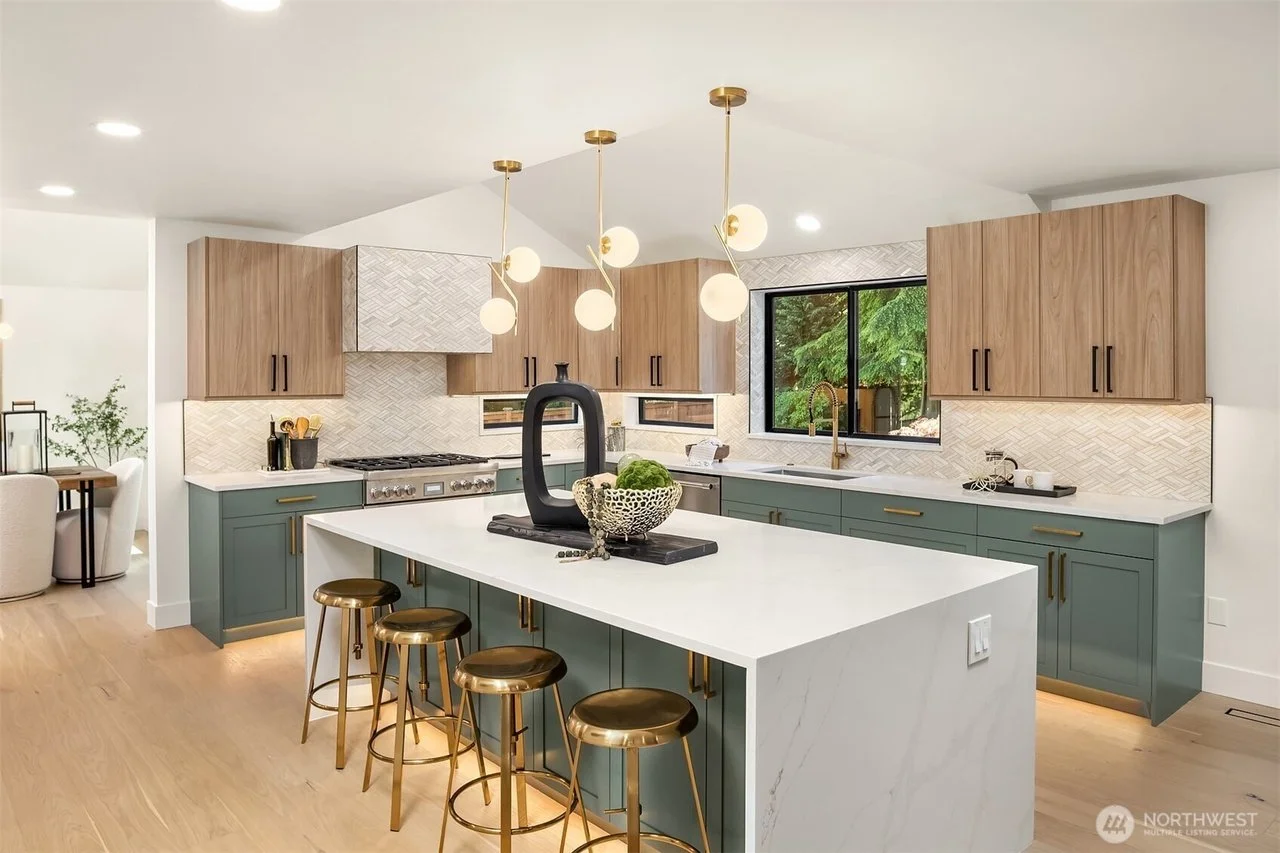 Modern kitchen with blue lower cabinets, wooden upper cabinets, white countertops, a large island with four gold stools, and a contemporary lighting fixture with multiple globe bulbs.