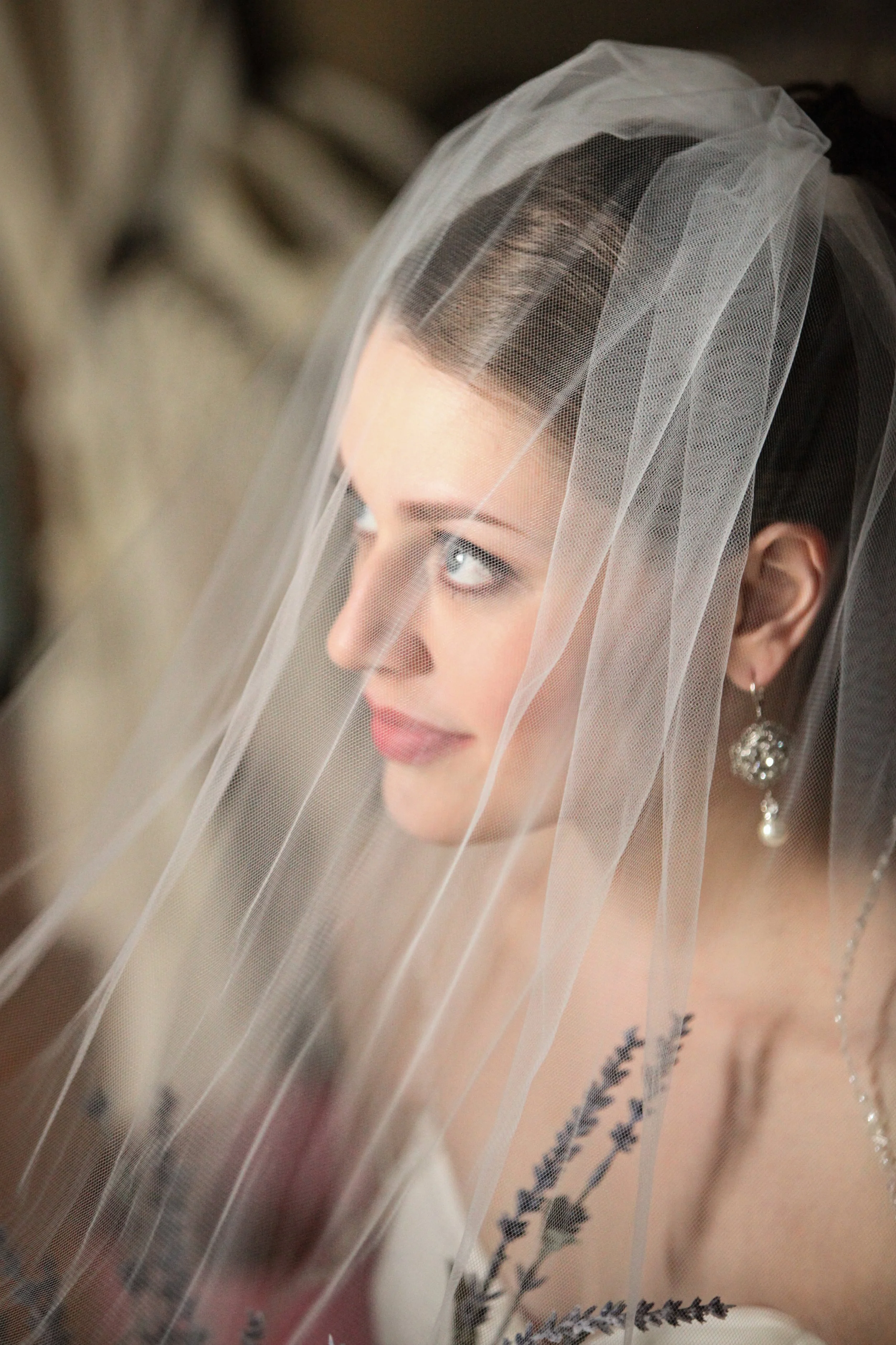 Close-up of a bride with a veil, earrings, and dark hair, looking to the side.