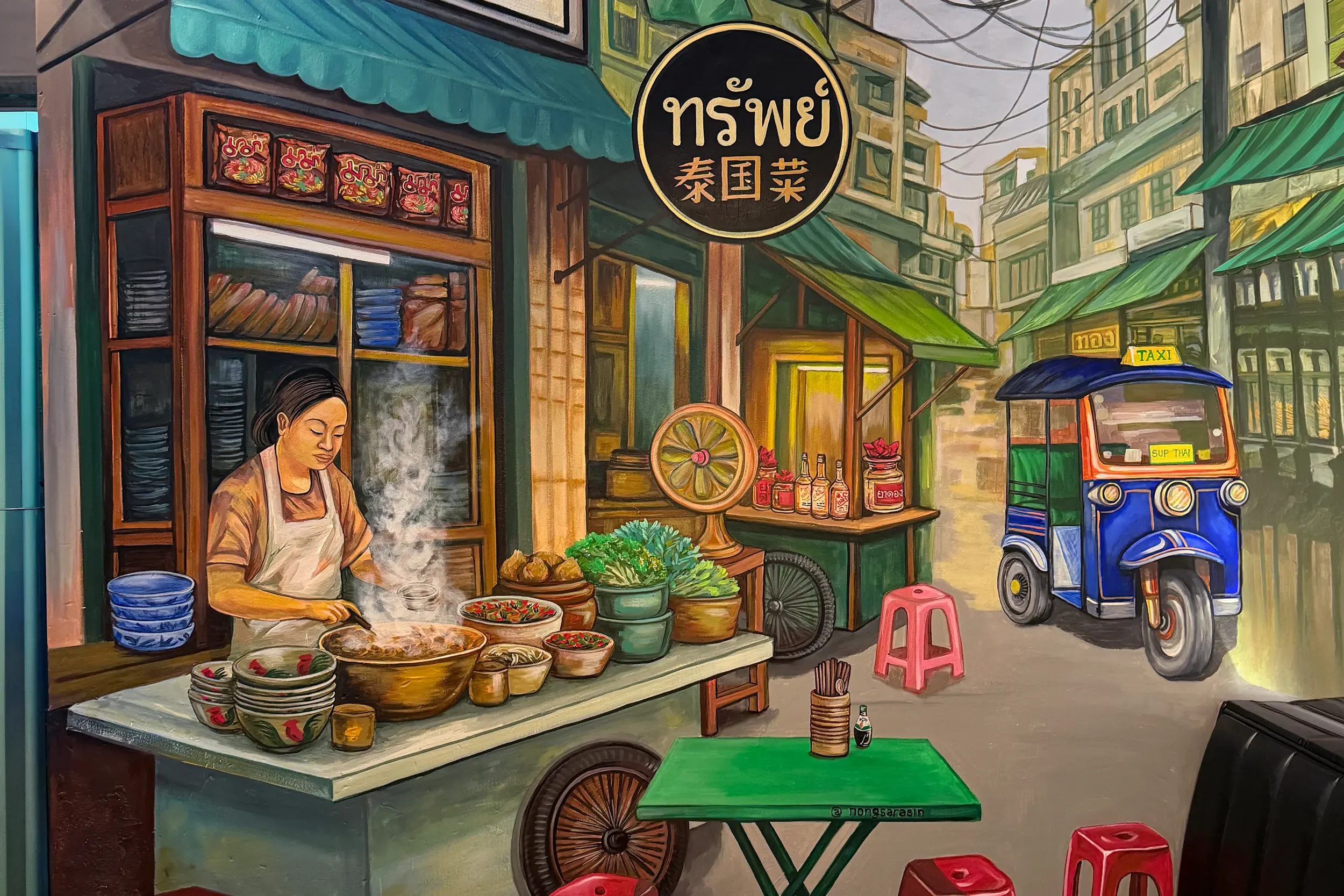 A colorful street scene mural featuring a woman preparing food at a street food stand, with bowls of ingredients, a market cart, a tuk-tuk, and buildings with green awnings in an urban setting.
