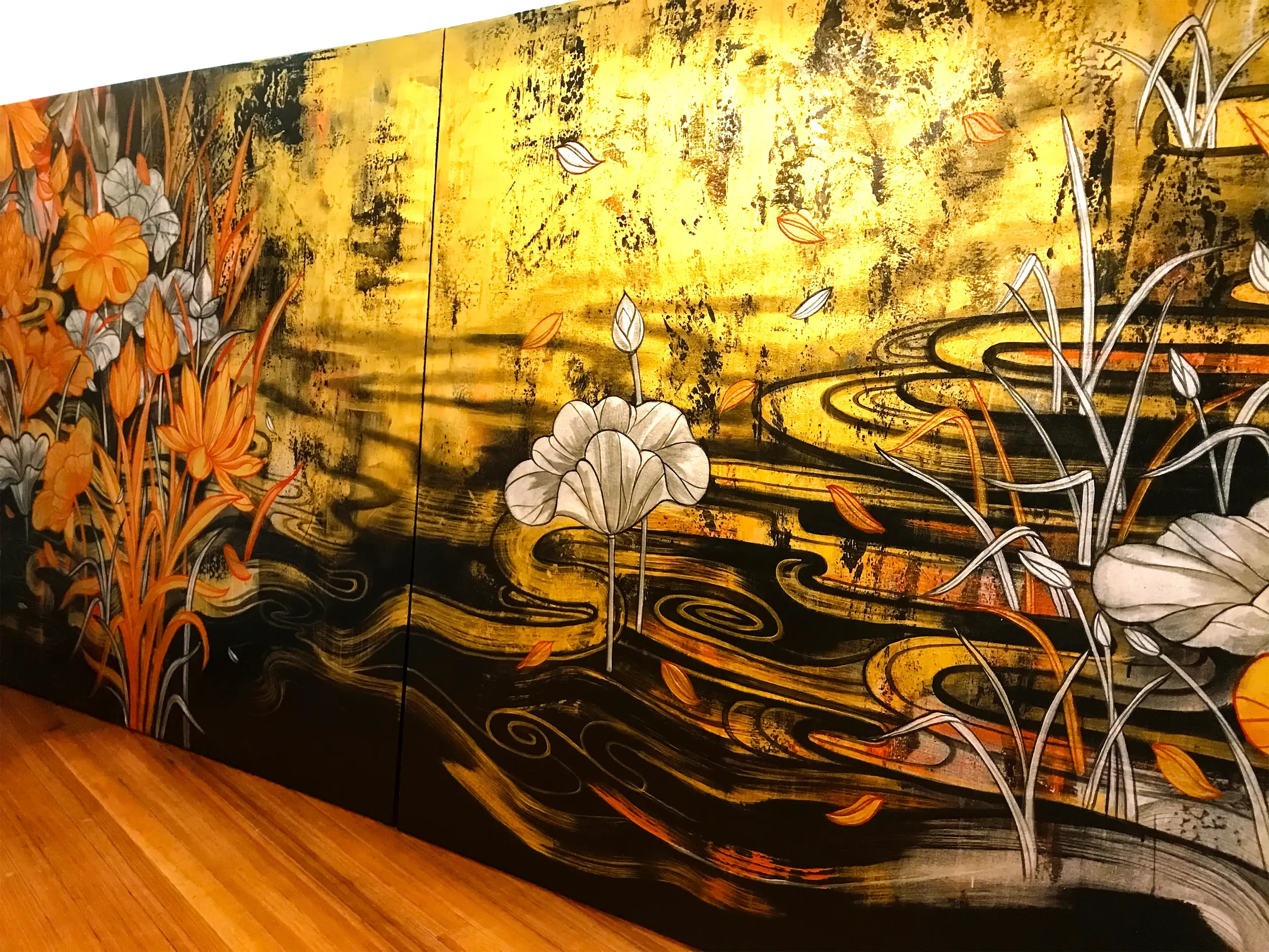 A large, decorative artwork featuring a gold background with black and orange floral illustrations and swirling design elements, displayed on a wall with a wooden floor below.