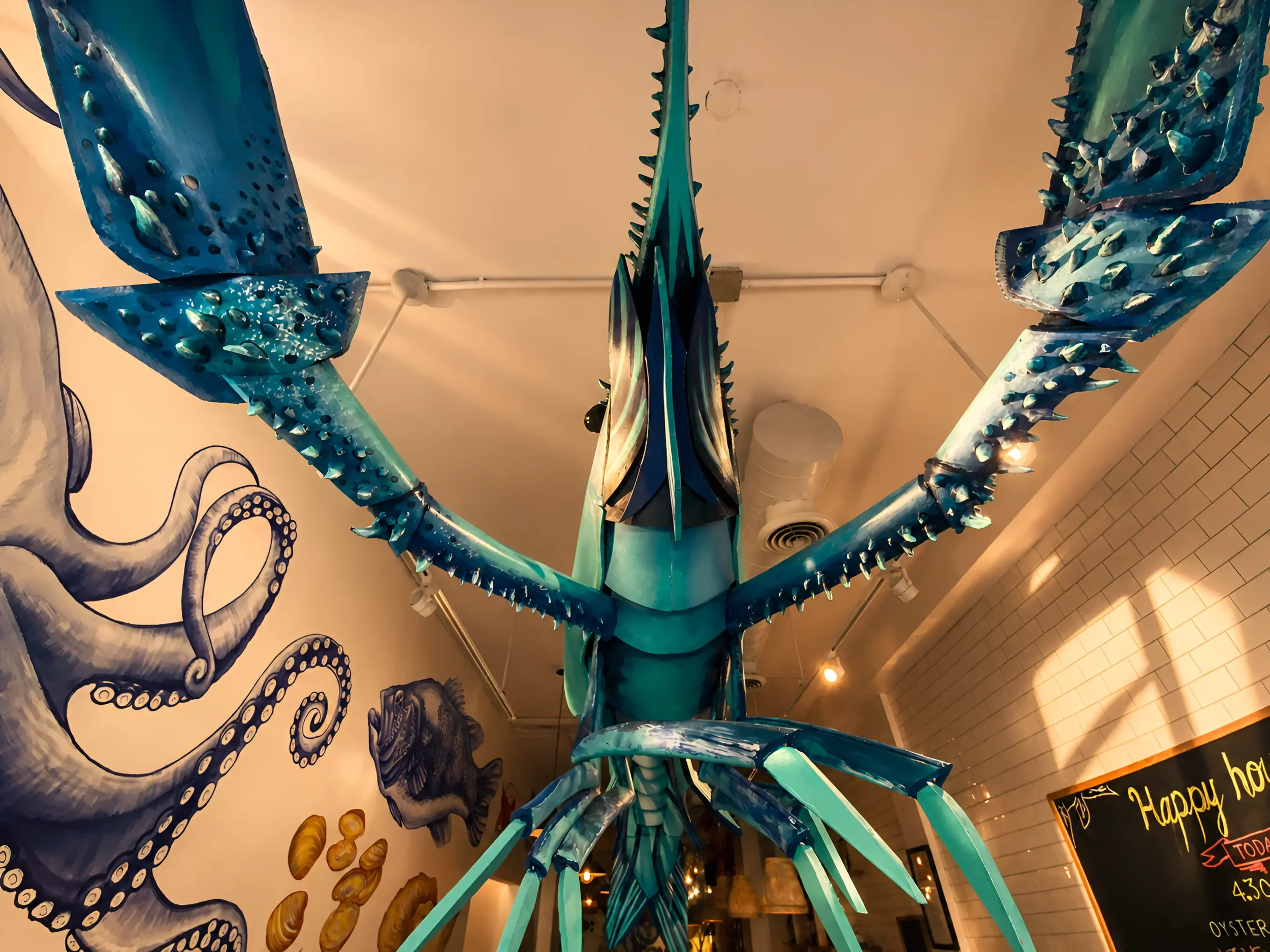 A large, colorful sculpture of an octopus with multiple extended tentacles, displayed indoors against a wall decorated with octopus-themed artwork and a chalkboard.