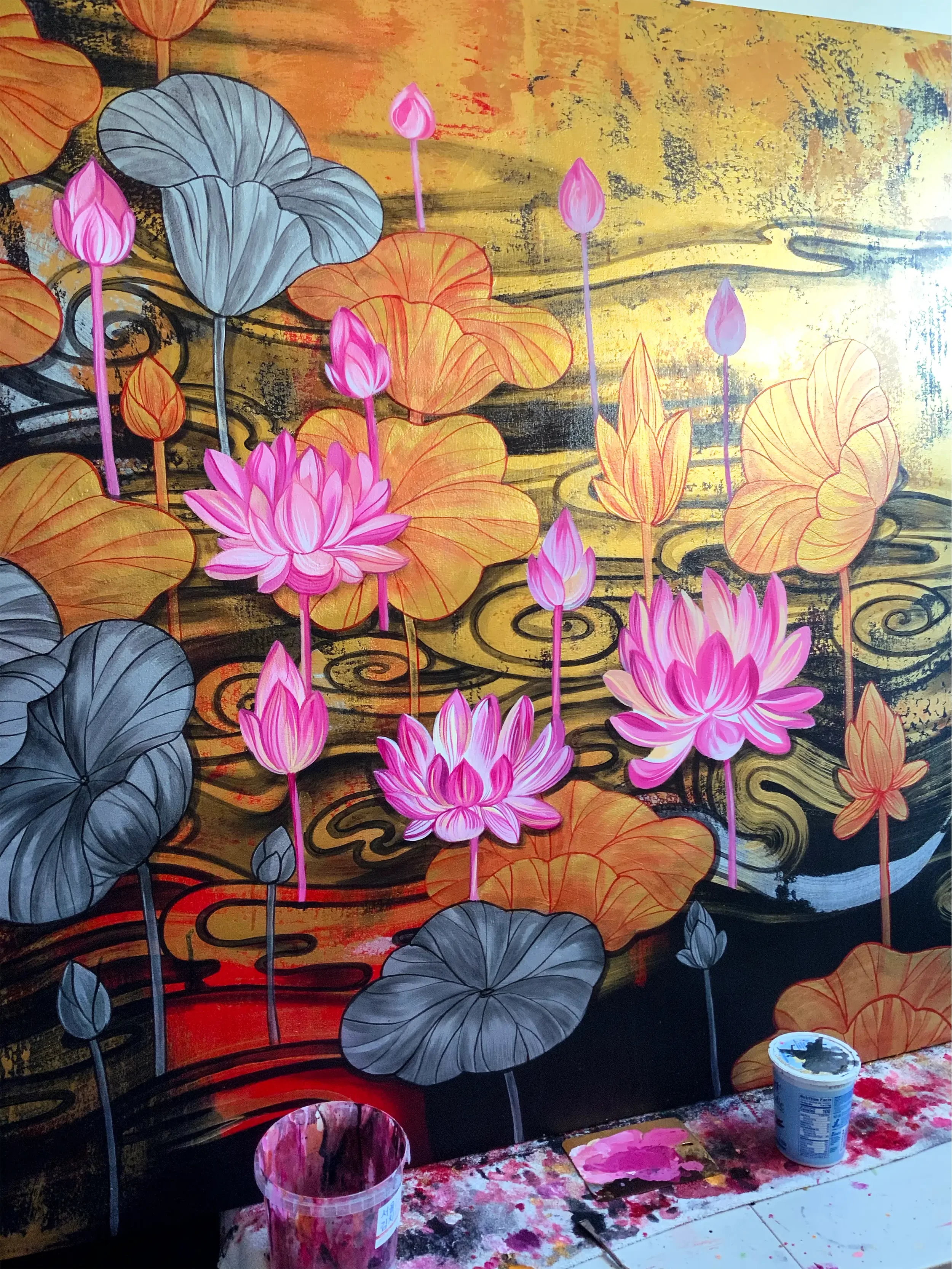 A colorful painting of lotus flowers with pink petals and dark green and gray leaves on a background of swirling gold and black patterns.