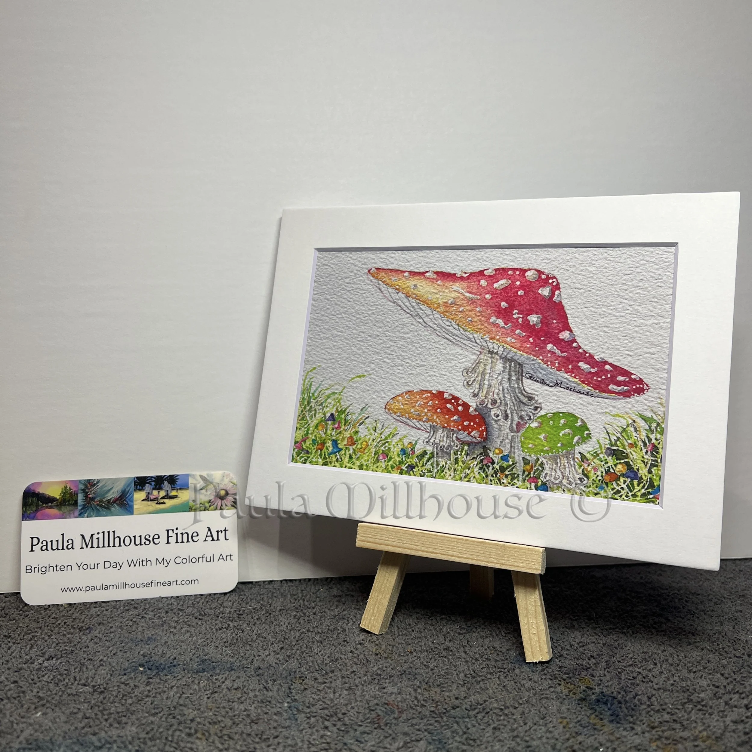 Whimsical woodland mushrooms growing on the forest floor with and grasses, watercolor painting by Paula Millhouse.