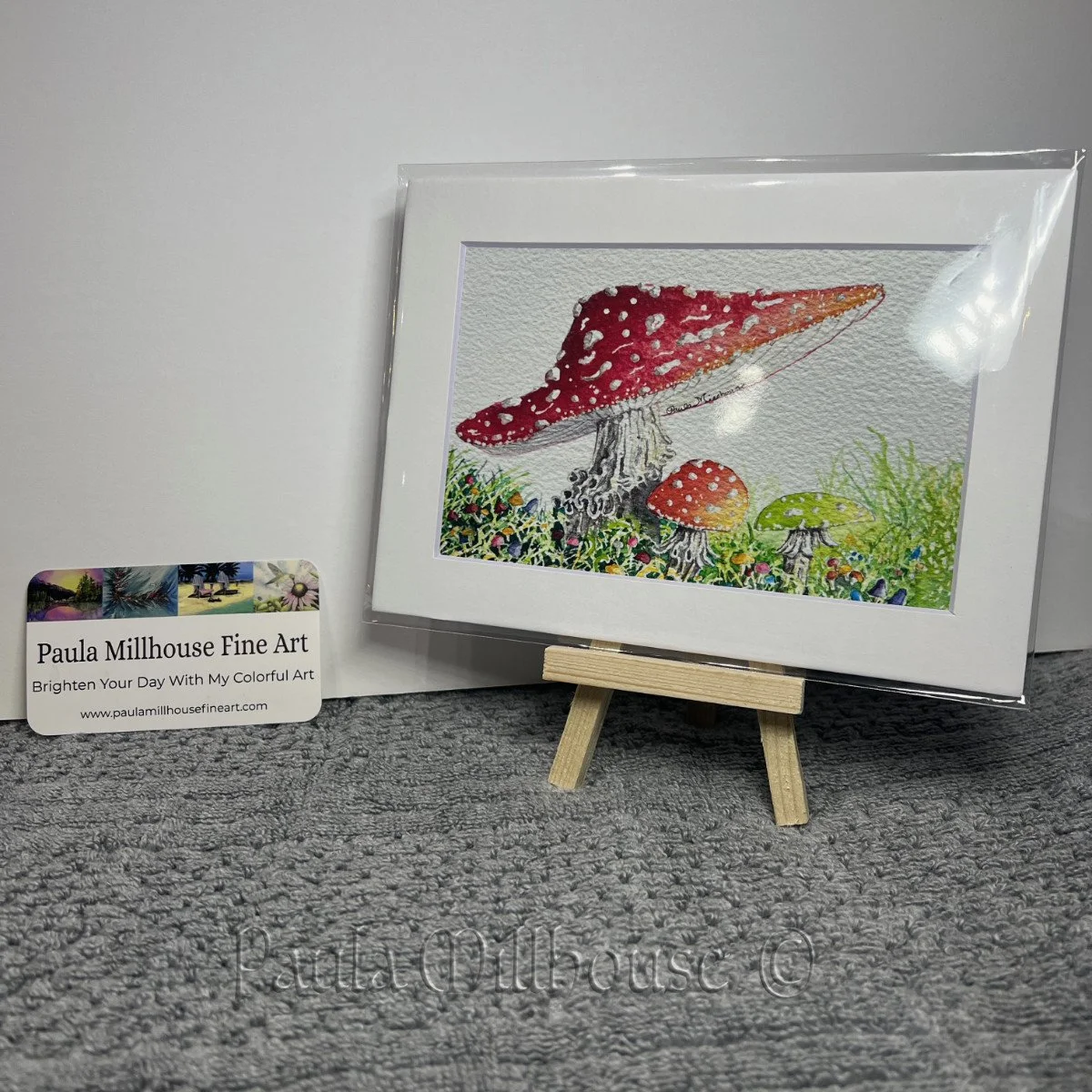 Three cheerful toadstool mushrooms celebrating in a woodland clearing, whimsical watercolor painting by Paula Millhouse.