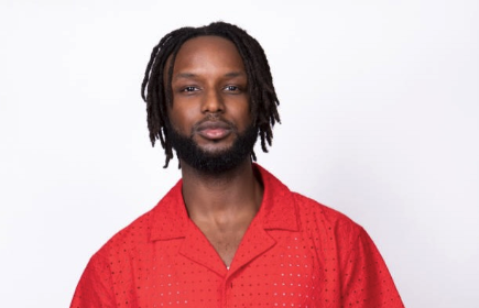 Portrait of Teddy Dumont with dreadlocks and a beard wearing a orange/red shirt
