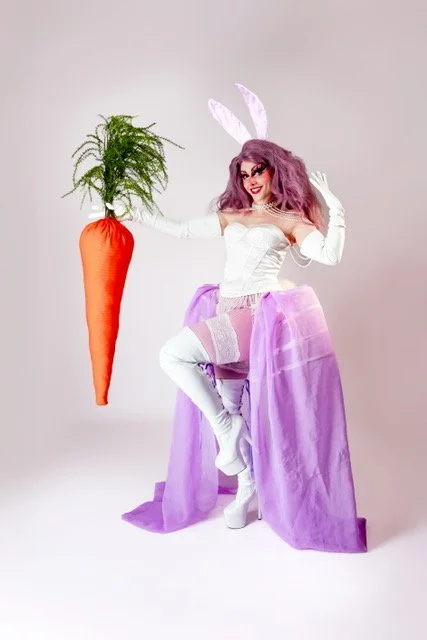 Mizrabelle in a white bunny costume and purple skirt, holding an oversized carrot