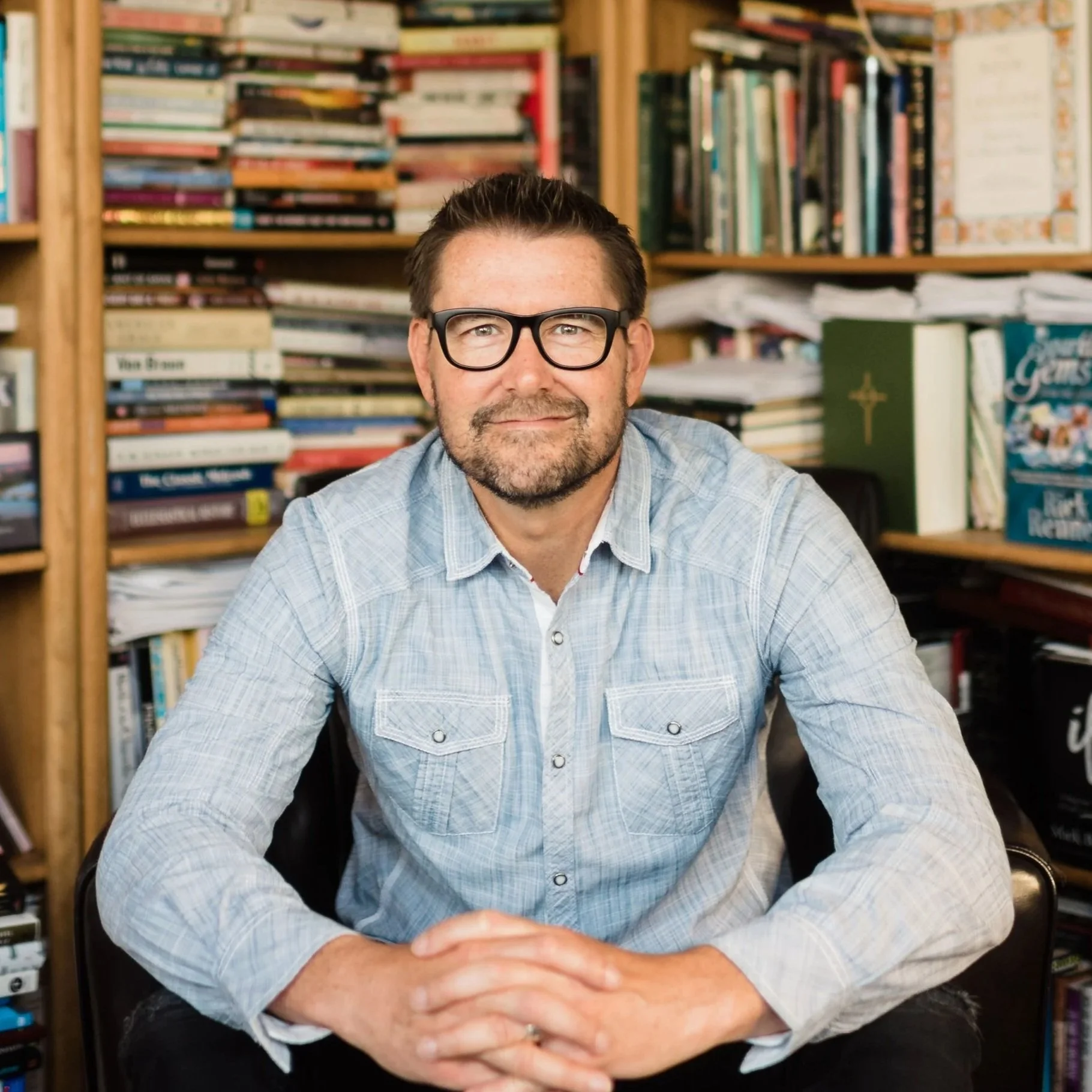A man with glasses and a beard, sitting at a desk in front of a bookshelf filled with books and papers. 2026 CCCU International Forum Speaker: Mark Batterson.