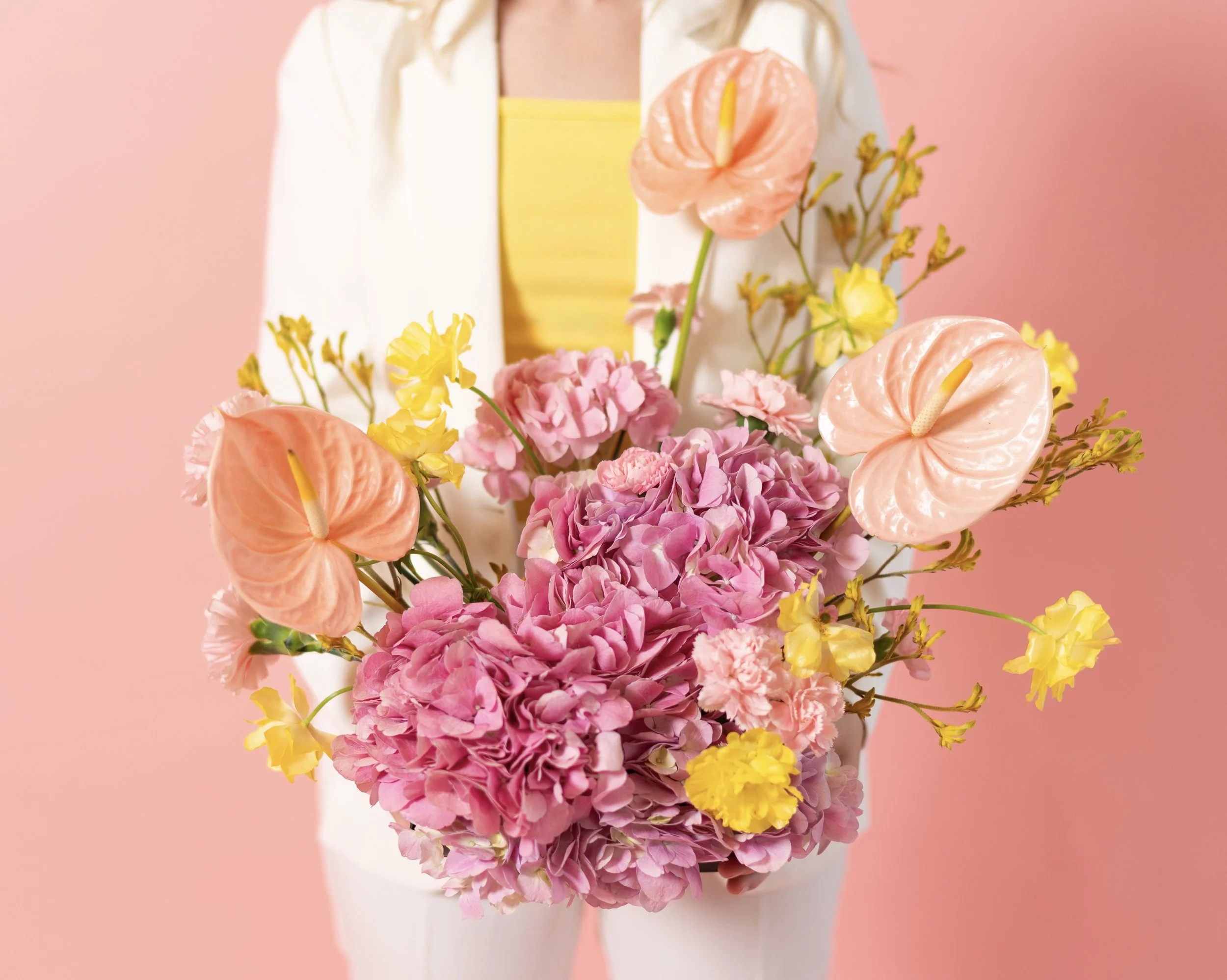 Person holding a bouquet of pink, yellow, and peach flowers against a pink background