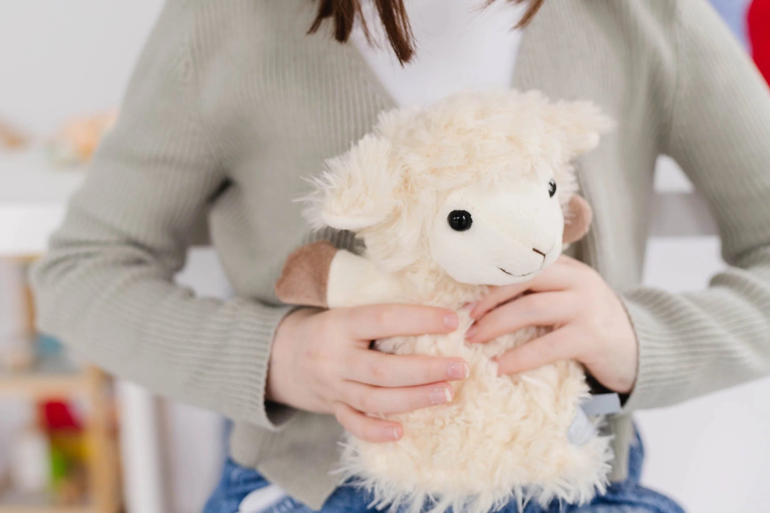 Person holding a plush sheep toy with a white woolly body and black eyes.