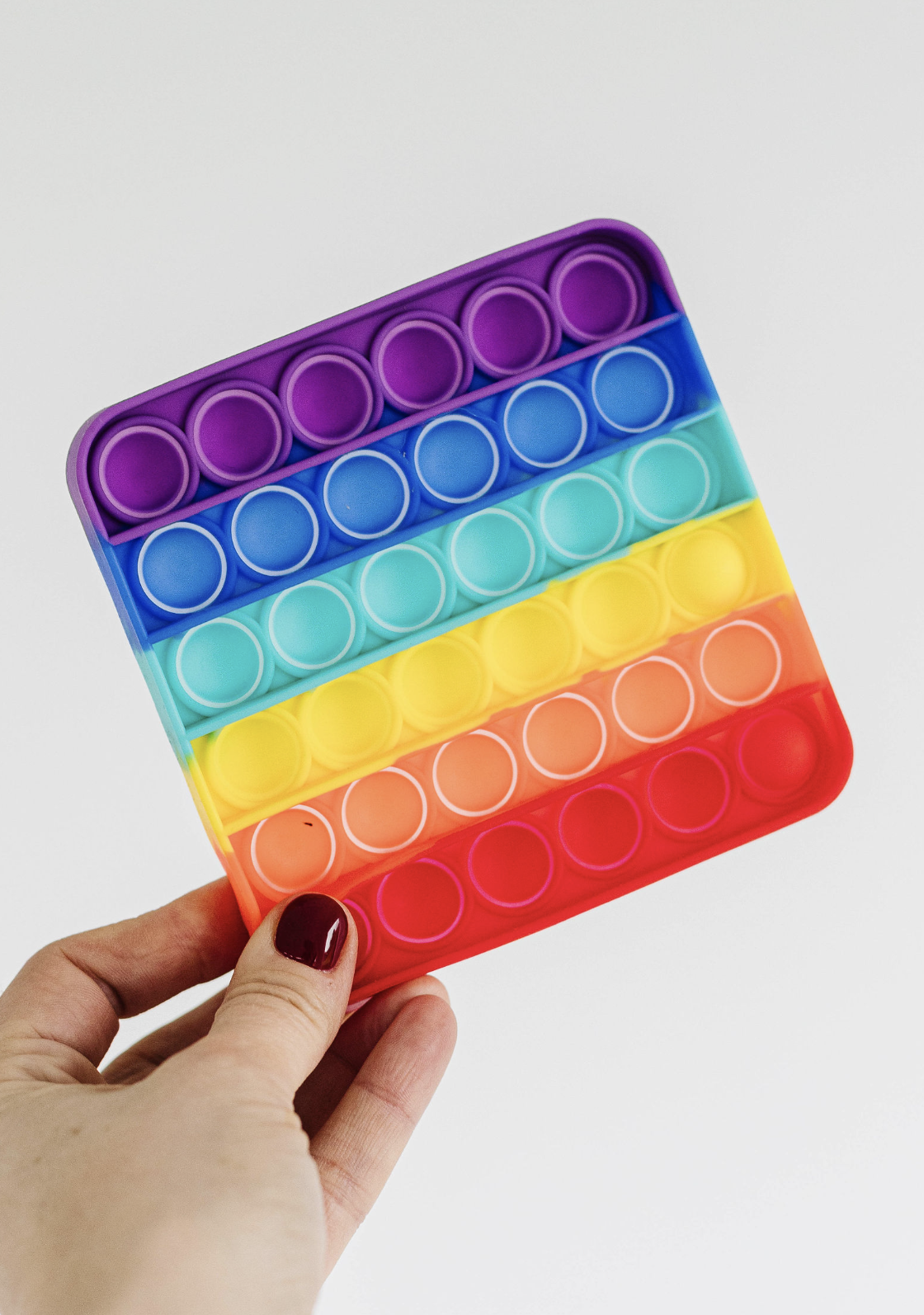 Hand holding a colourful silicone fidget popper with rainbow pattern.
