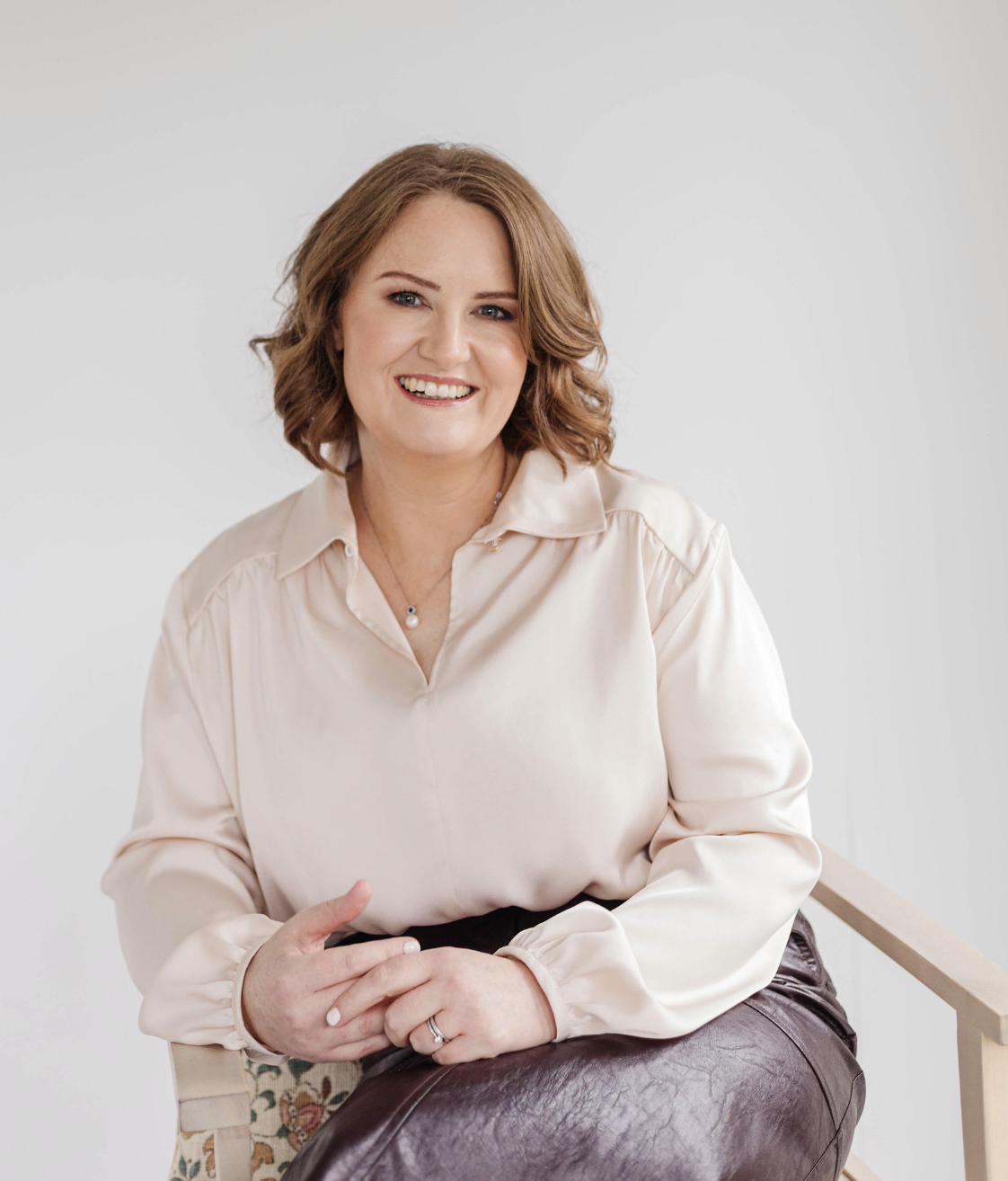 A smiling woman (Jill) with shoulder-length brown hair, wearing a cream blouse, sitting on a chair against a plain light background.