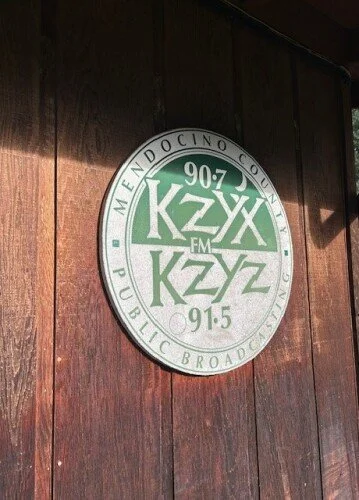 KZYX radio station logo on wooden wall featuring KZYX and KZYZ, frequencies 90.7, 91.5, with the words Mendocino County and Public Broadcasting.
