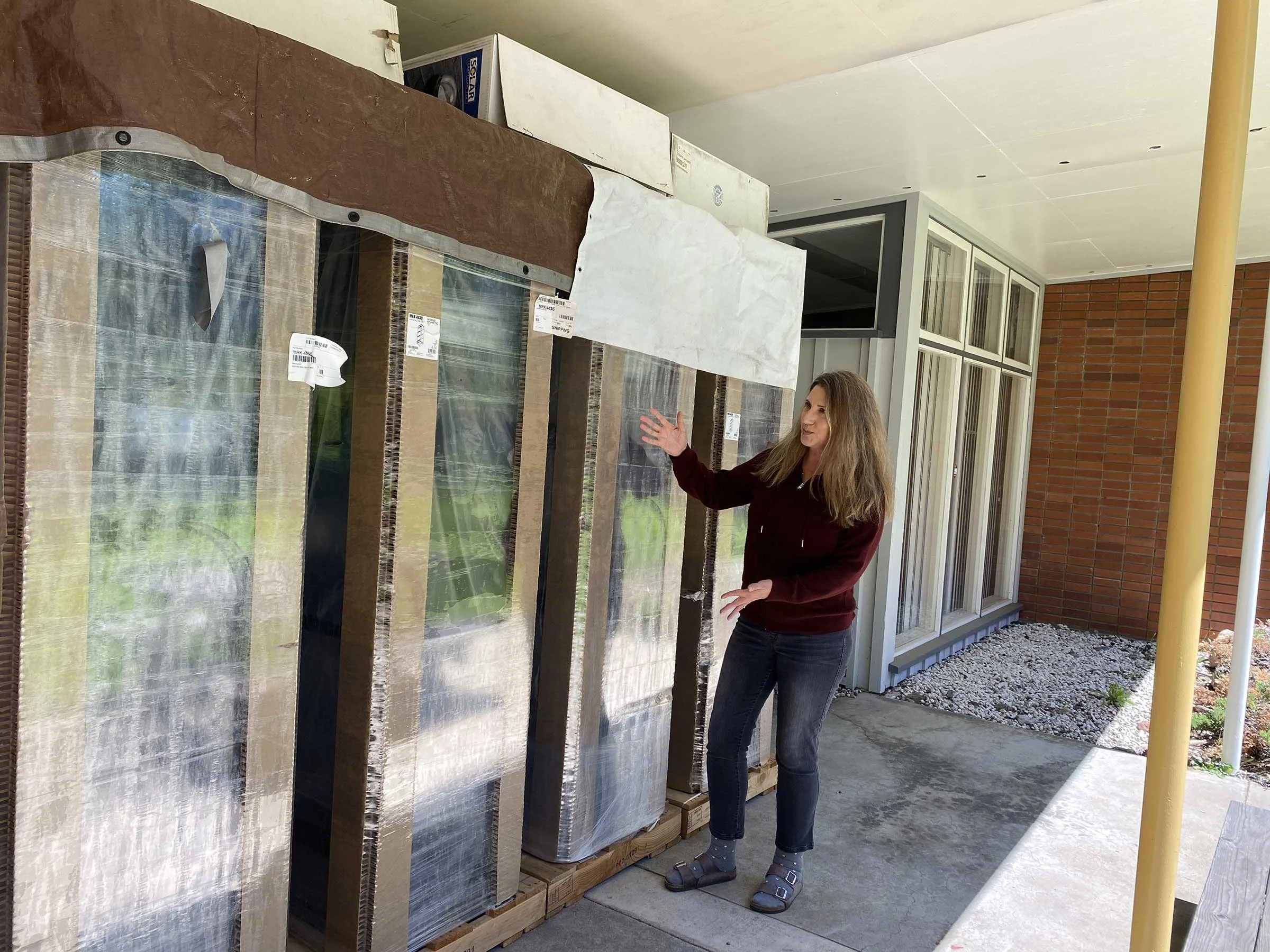 Woman standing outdoors next to large wrapped containers holding new racks for broadcasting equipment at KZYX Clay Street headquarters.
