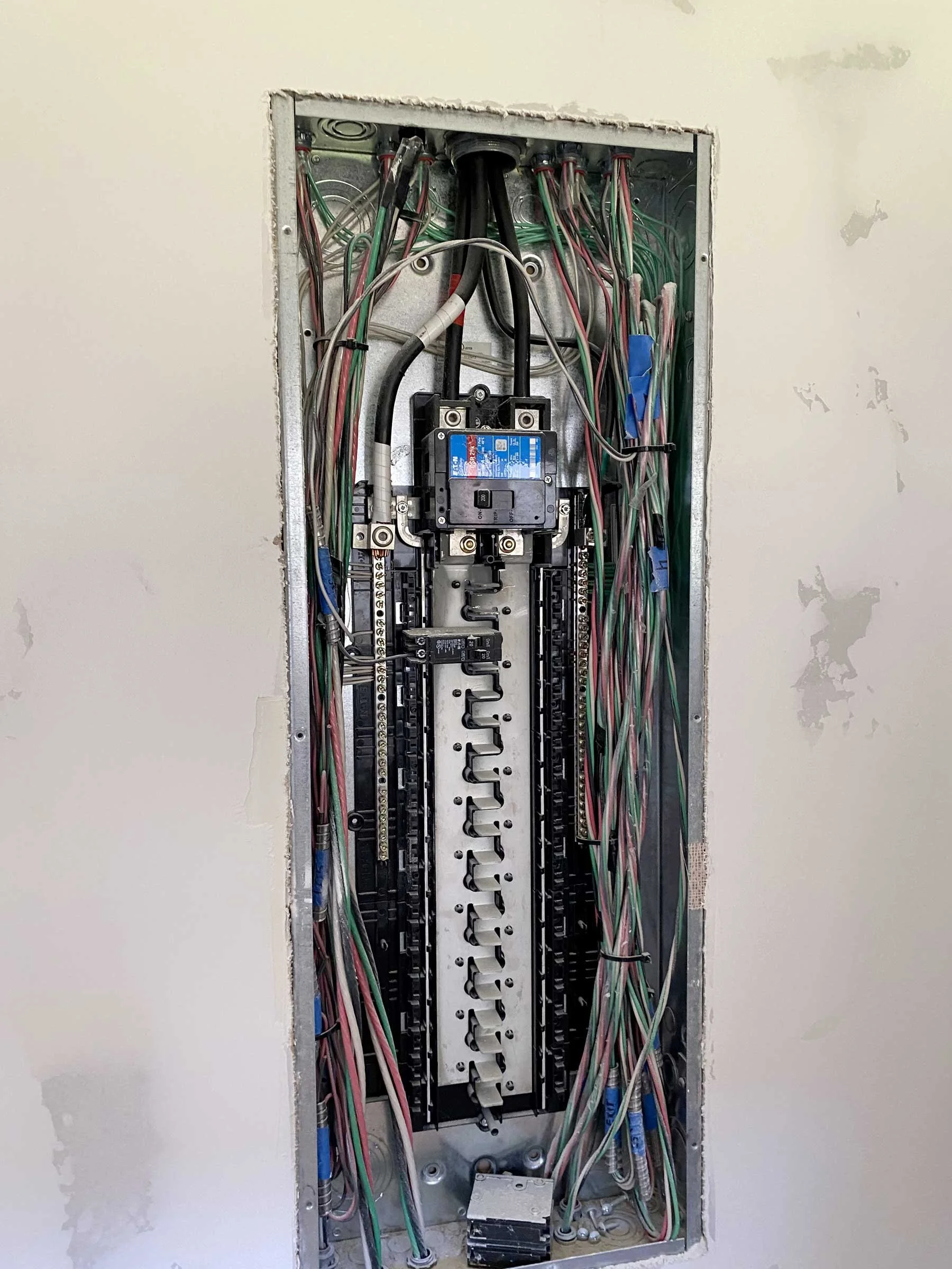 An electrical breaker panel with numerous wires connected inside a wall.