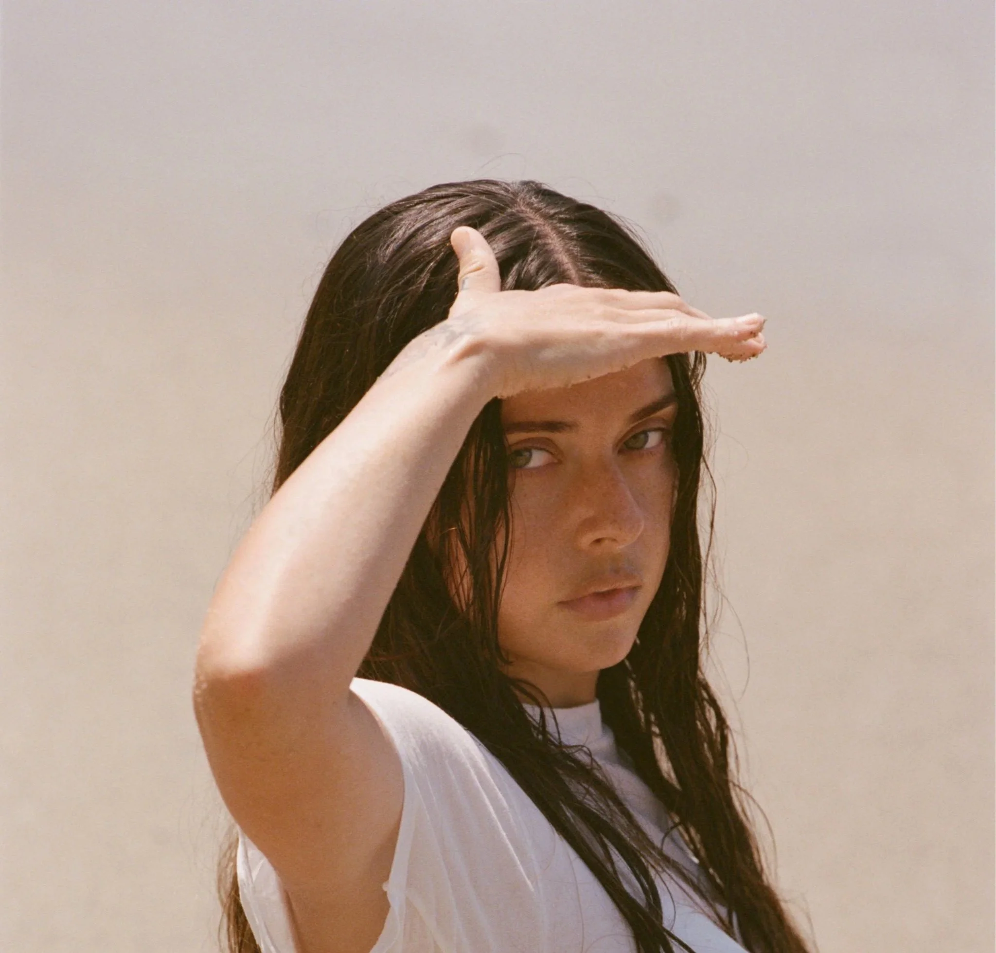 Close-up black and white photo of a woman with long dark hair, gazing with a neutral expression, holding a glass with a straw in her lips.